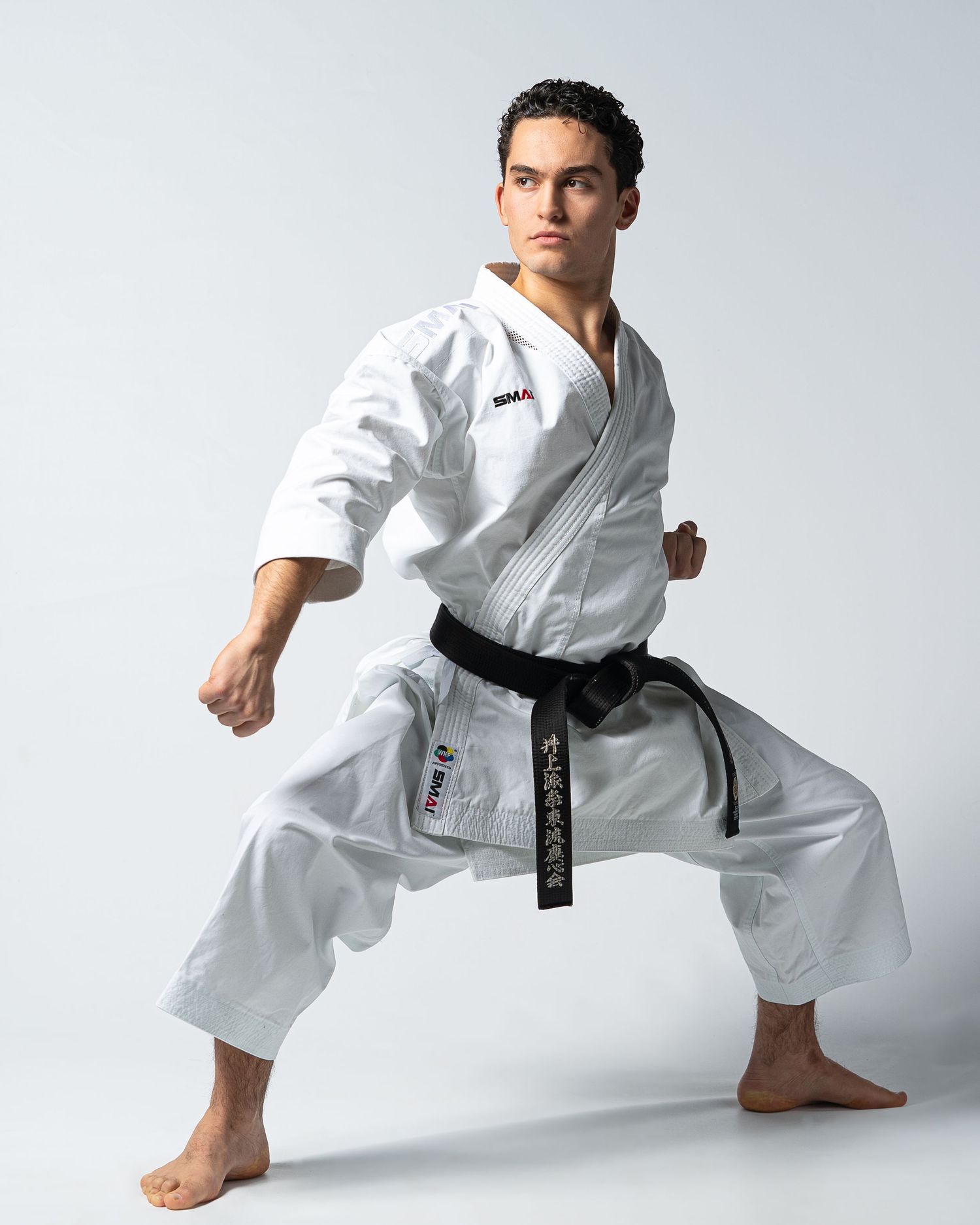 Athletic person in white karate uniform performing traditional martial arts stance against light background.