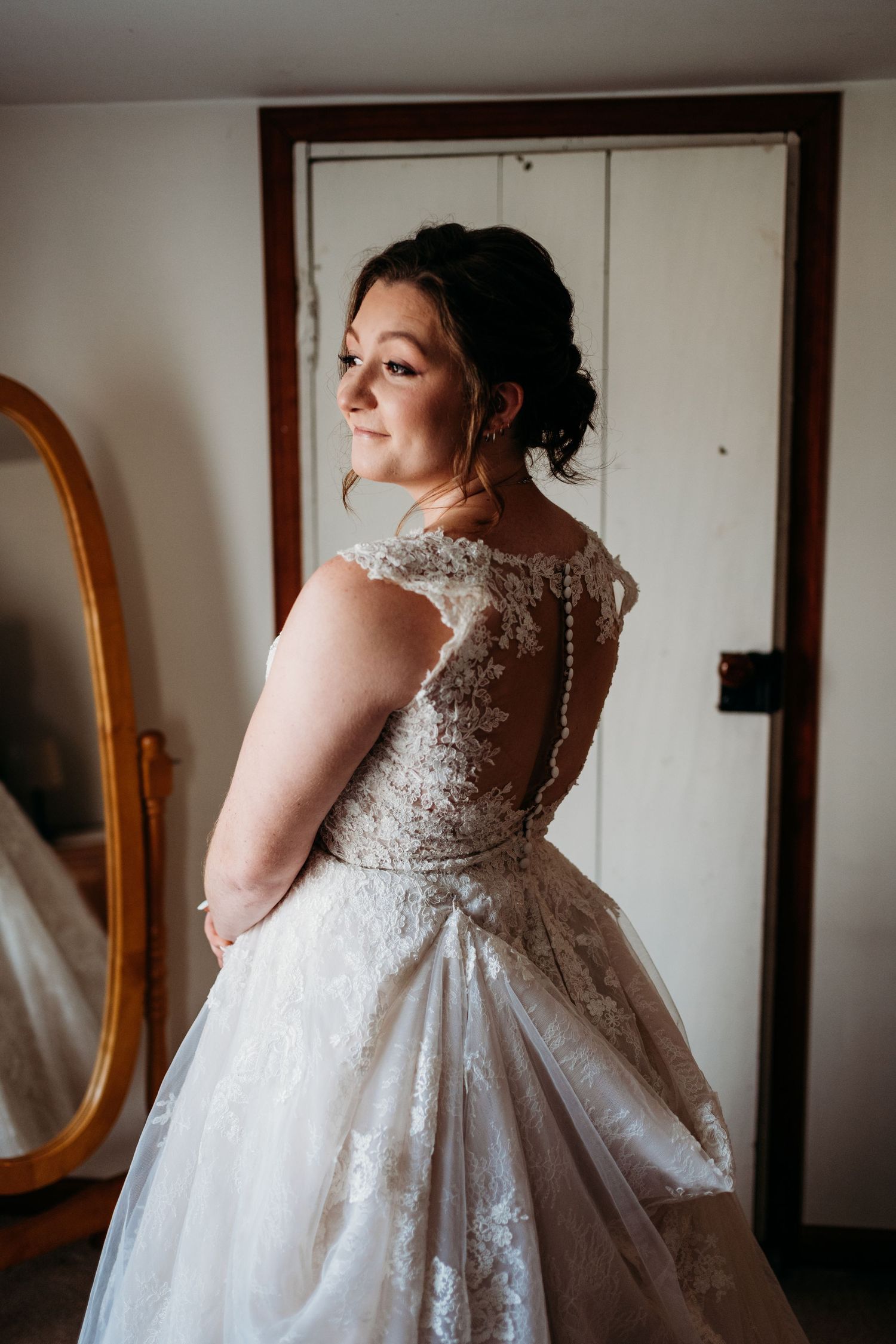A wedding dress with intricate lace details and an elegant buttoned back is showcased in soft natural lighting.