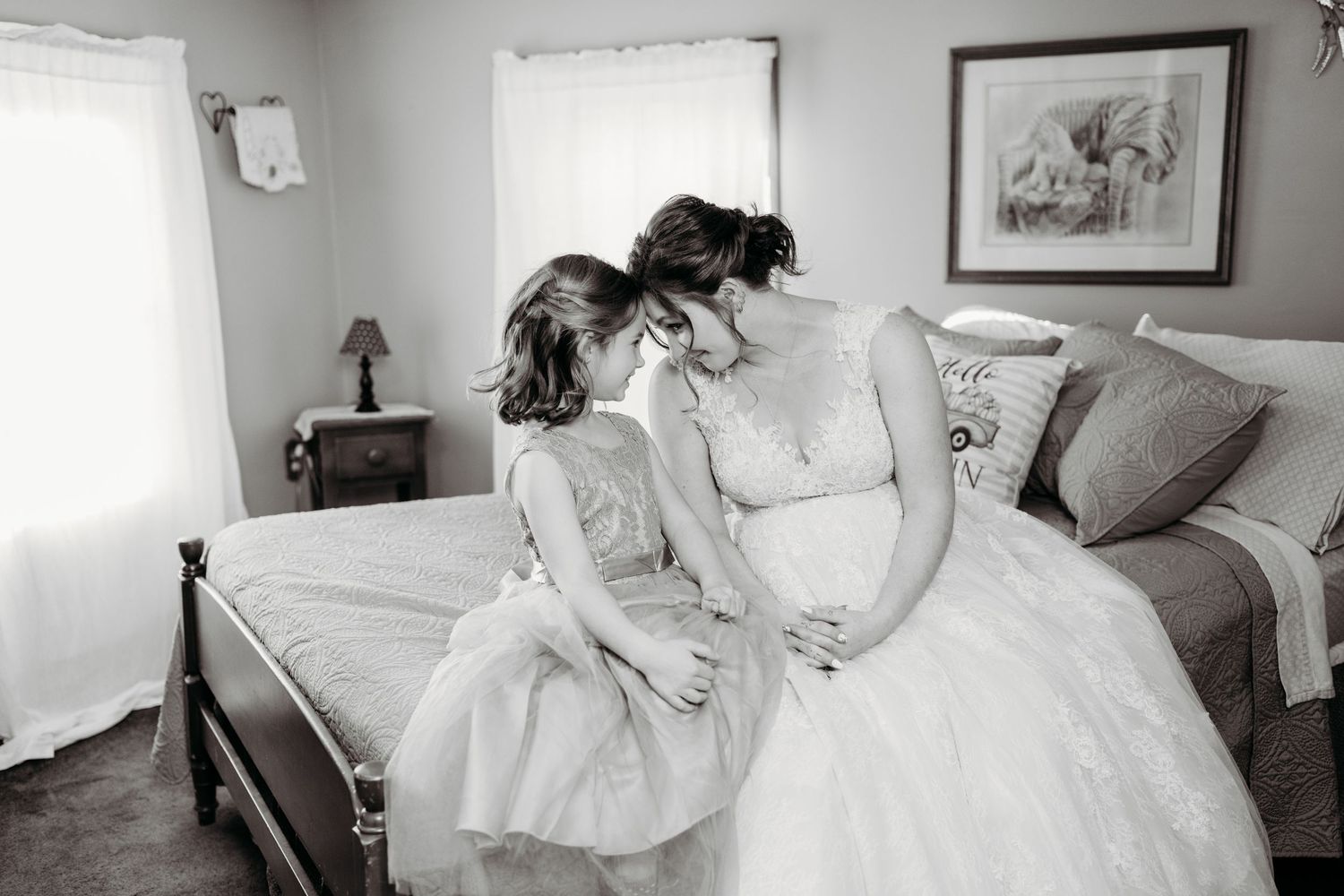 Black and white photo showing two people in light dresses sharing a tender moment together in a bedroom setting.
