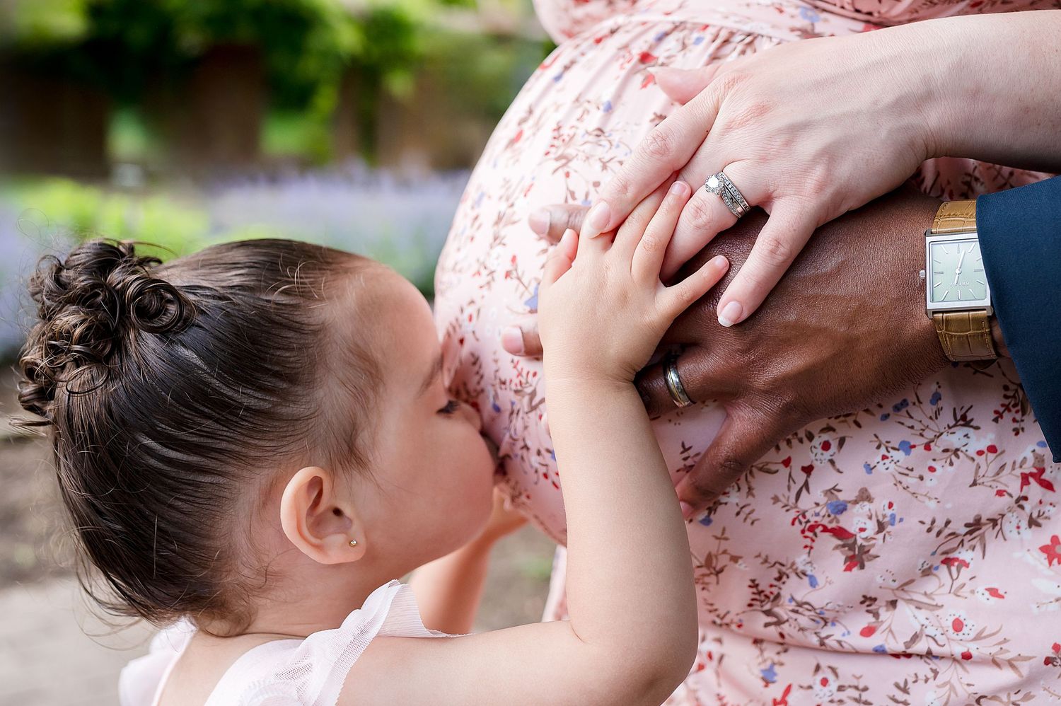 A young child leaning forward to kiss a pregnant woman's belly while holding it with their hands.