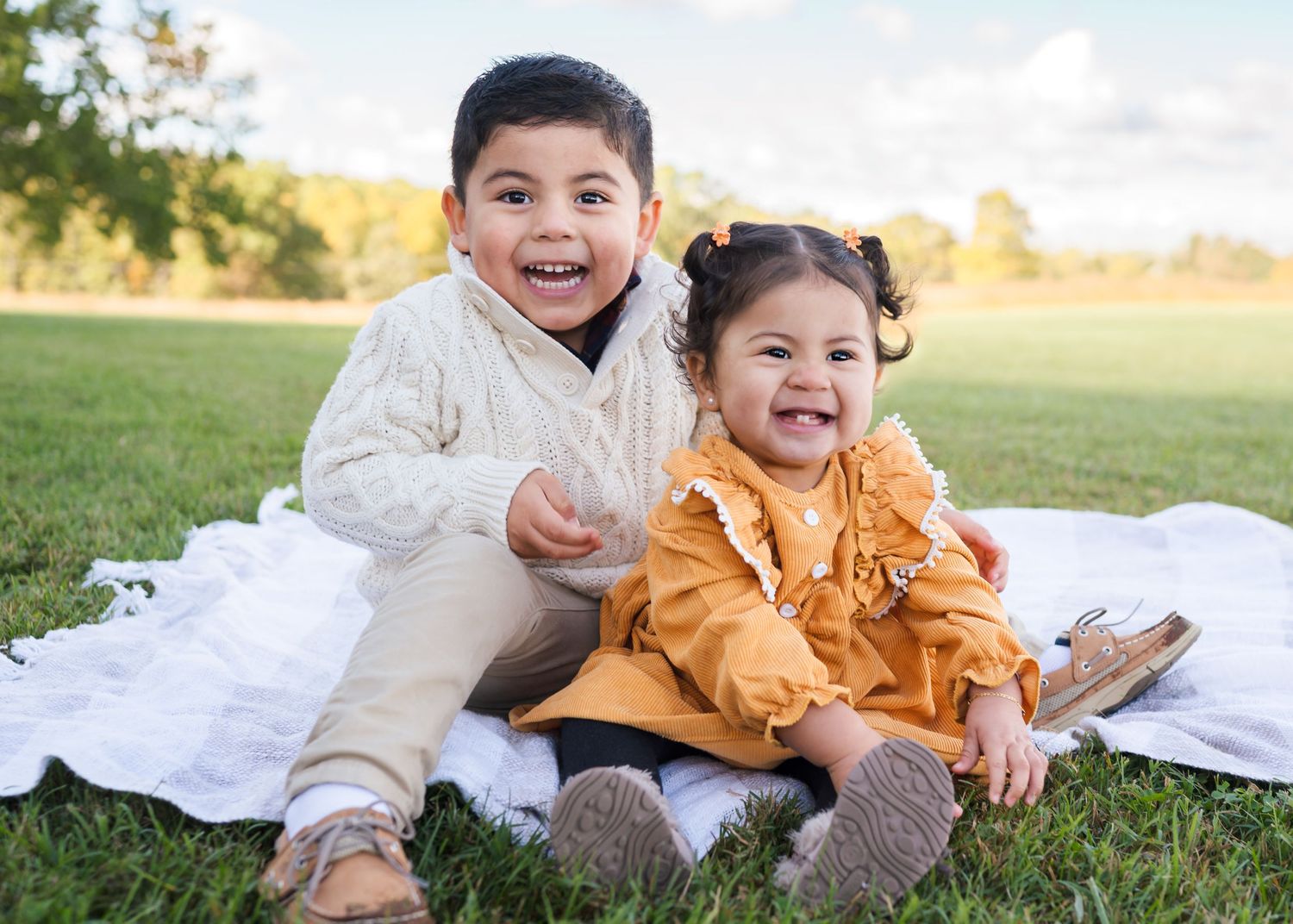A group enjoying playful moments together on a blanket in a sun-lit grassy field during golden hour.