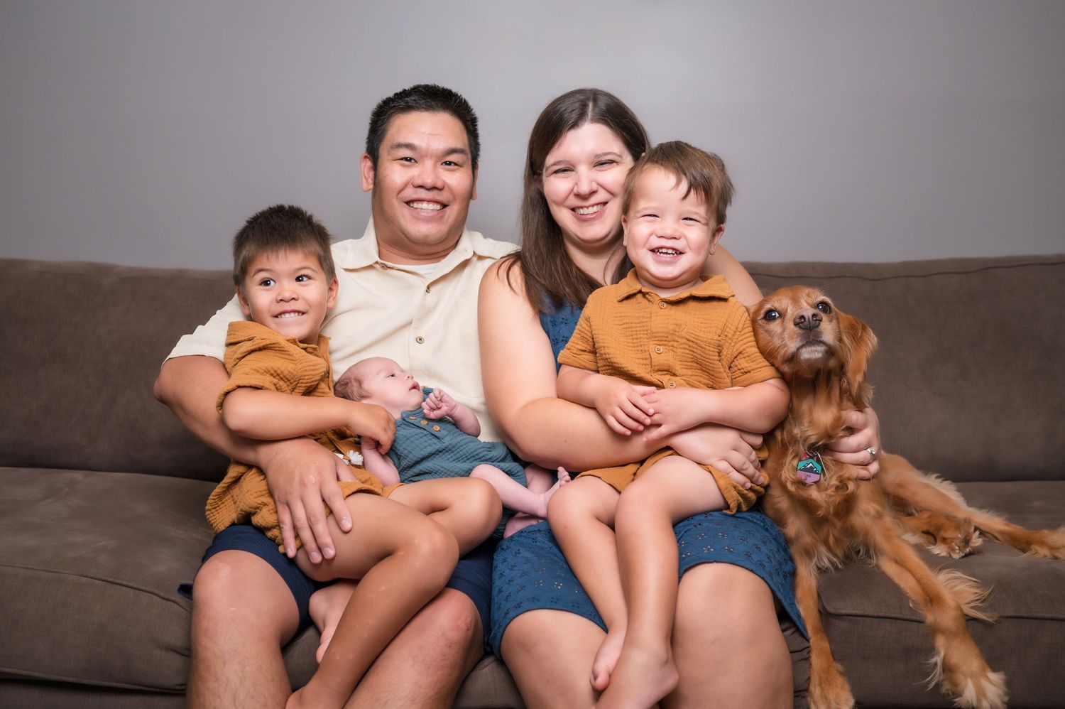 A happy family sits together on a brown couch with their golden retriever dog.