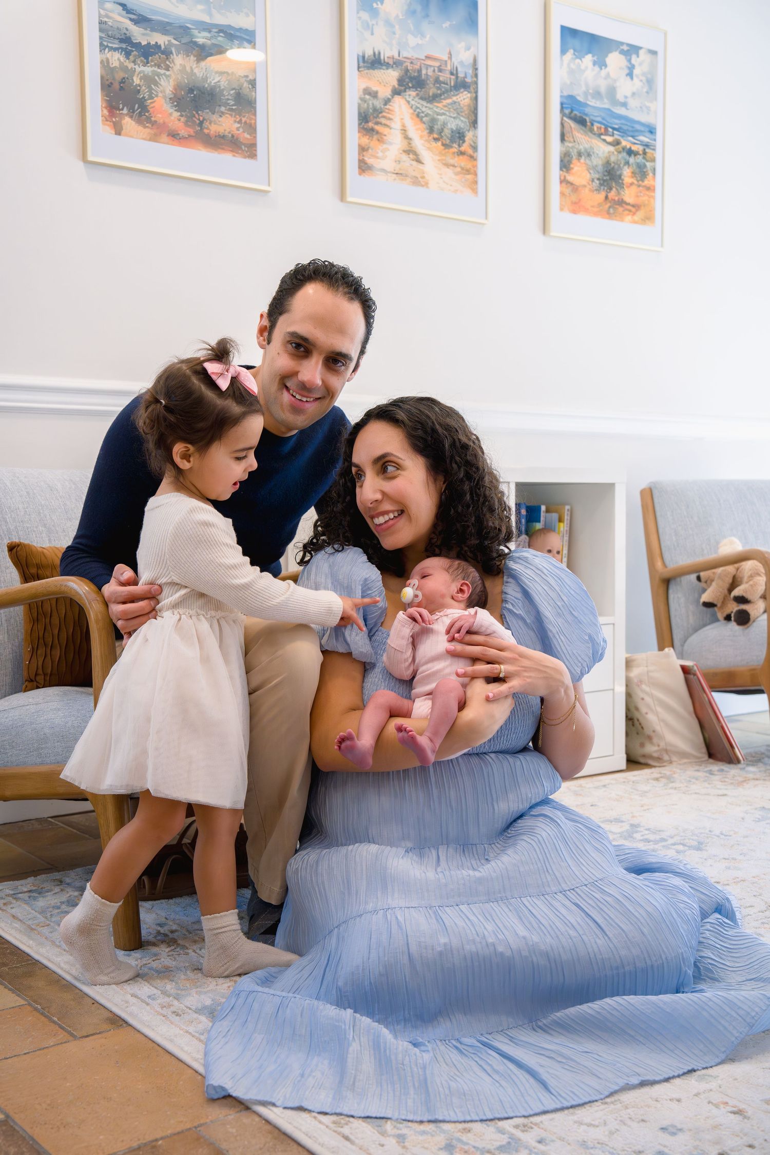 Happy family of four poses indoors, parents with toddler girl and newborn baby, in Gaithersburg, MD