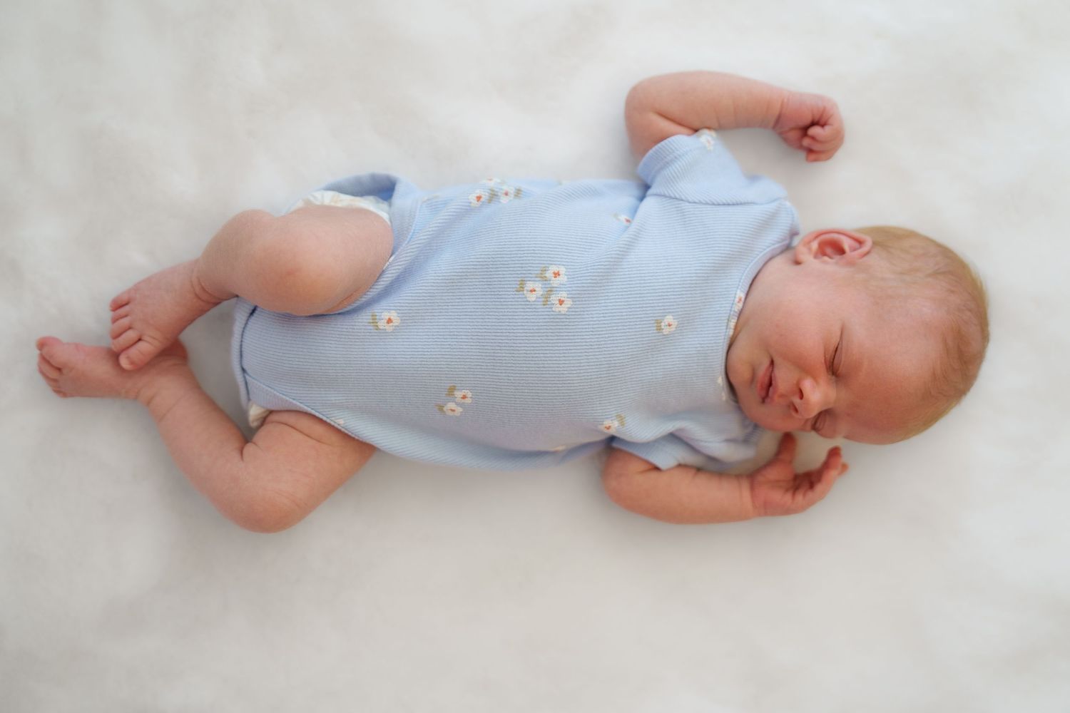 Sleeping newborn baby in a light blue floral romper lying on a soft white blanket, during a newborn session in Frederick, MD