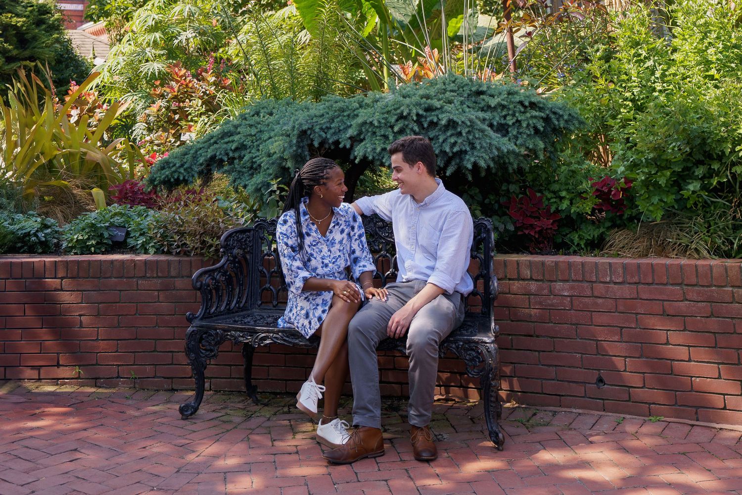 A couple shares an intimate moment while sitting on brick steps surrounded by lush garden foliage during an engagement session in DC