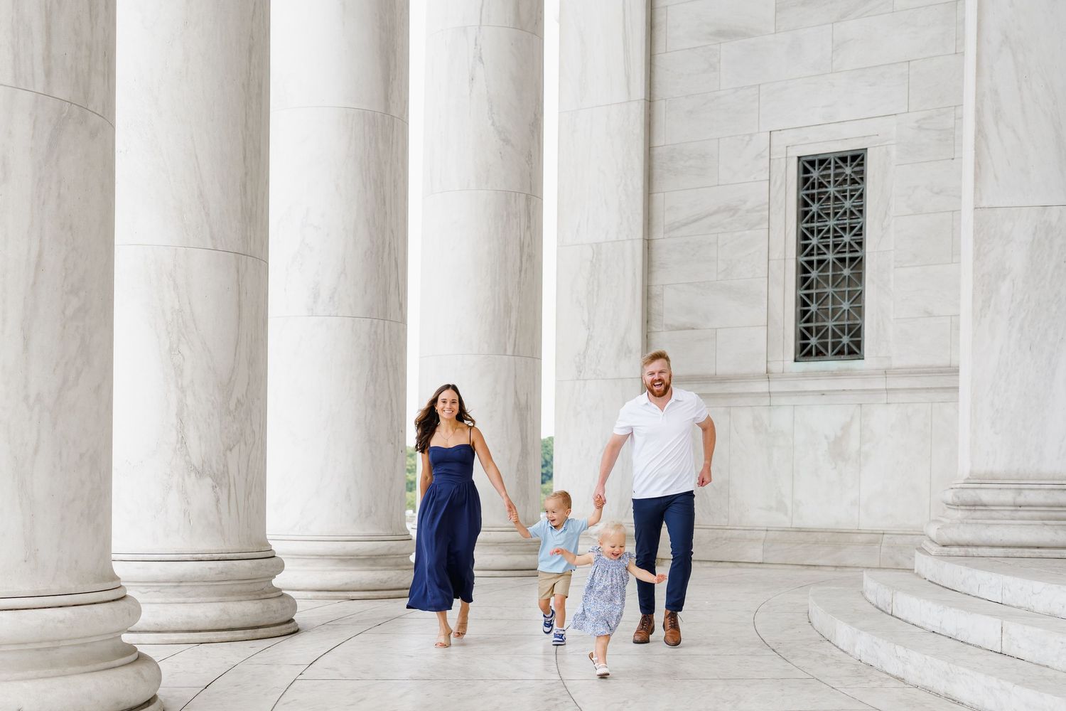 Family of three walking hand-in-hand between white marble columns at a grand monument at the Jefferson Memorial in Washington DC
