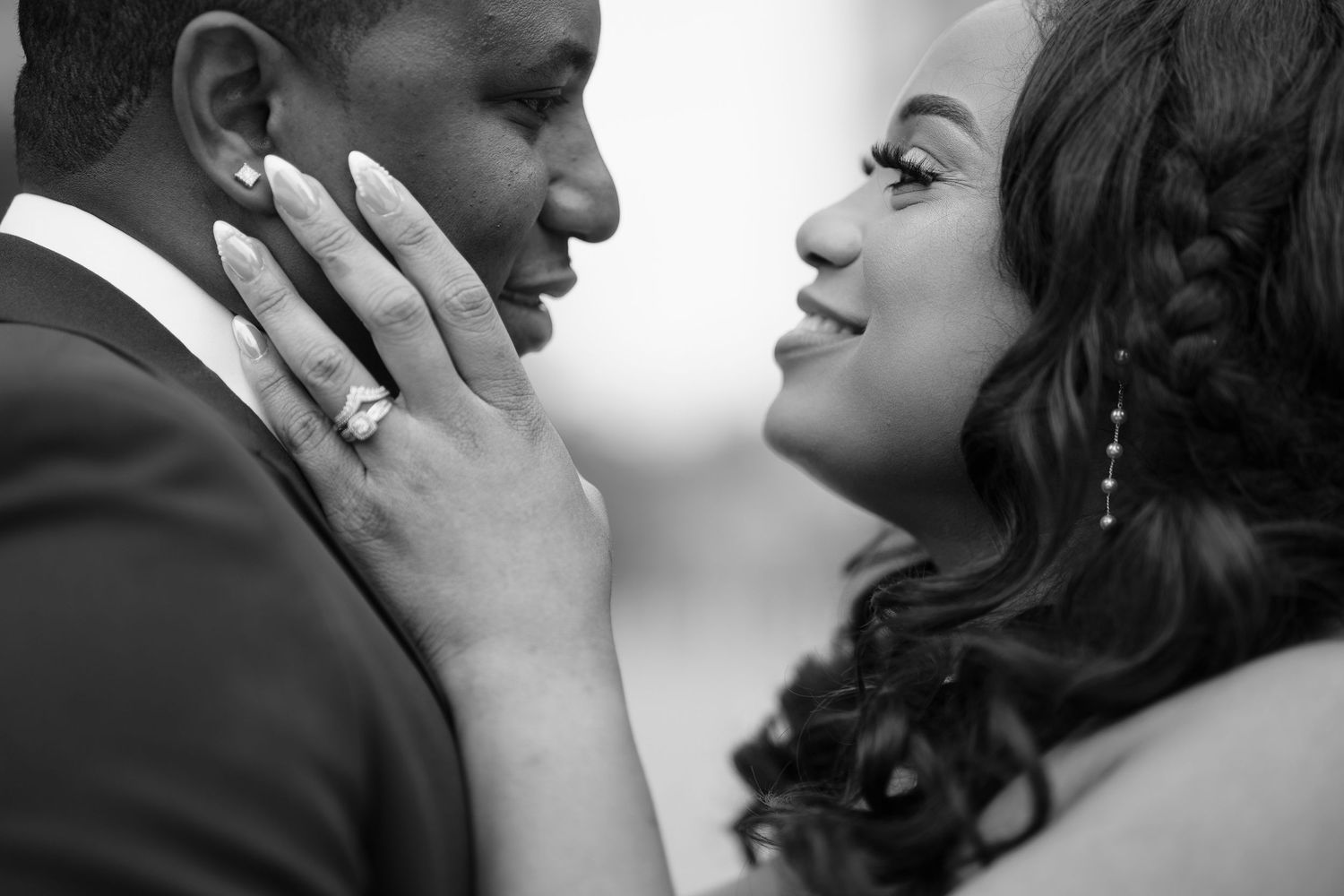 Black and white photo of a couple in a romantic moment, woman smiling and touching mans face, wearing elegant attire.