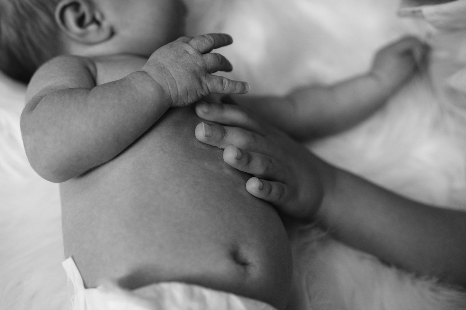 Close up black and white image of baby hands and torso resting on soft white fabric.
