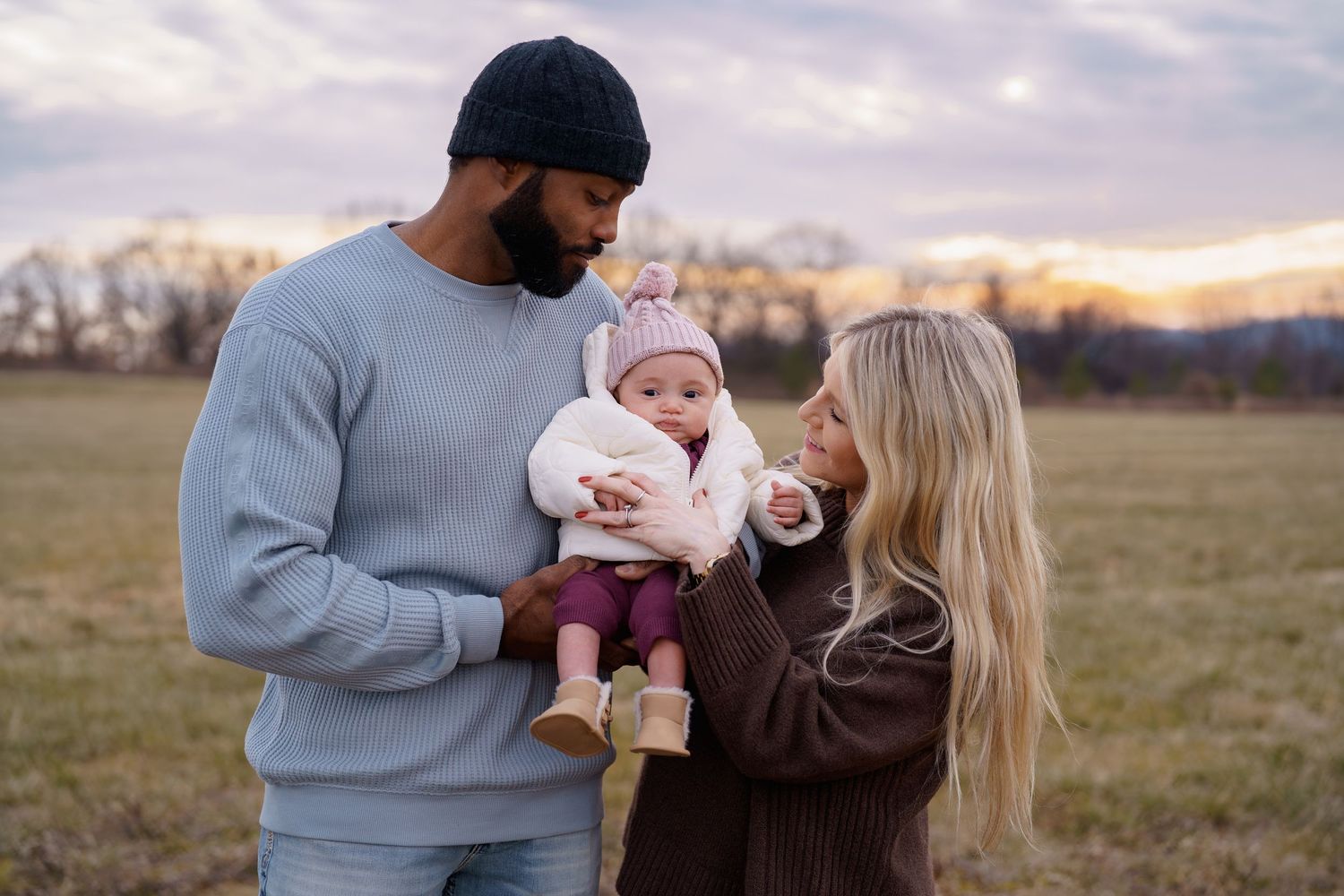Interracial family with mother, father, and baby girl posing outdoors at sunset in a grassy field, in Frederick, MD