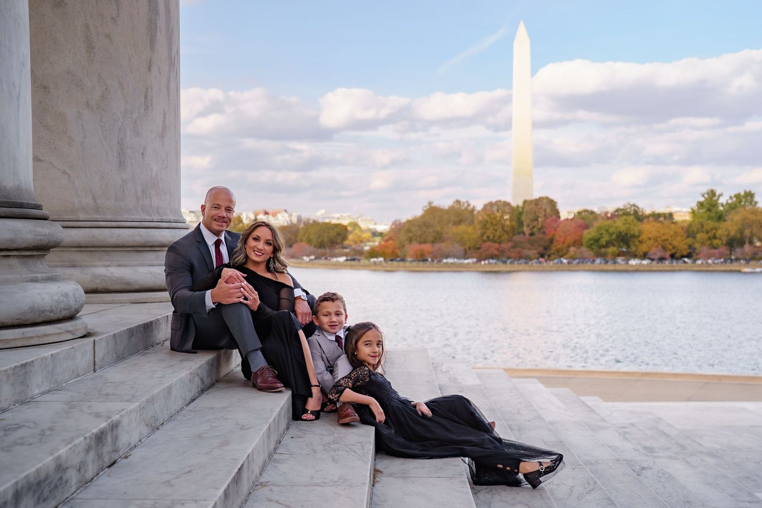 Family of four posing on steps near the Washington Monument and Tidal Basin in Washington D.C. on a sunny autumn day.