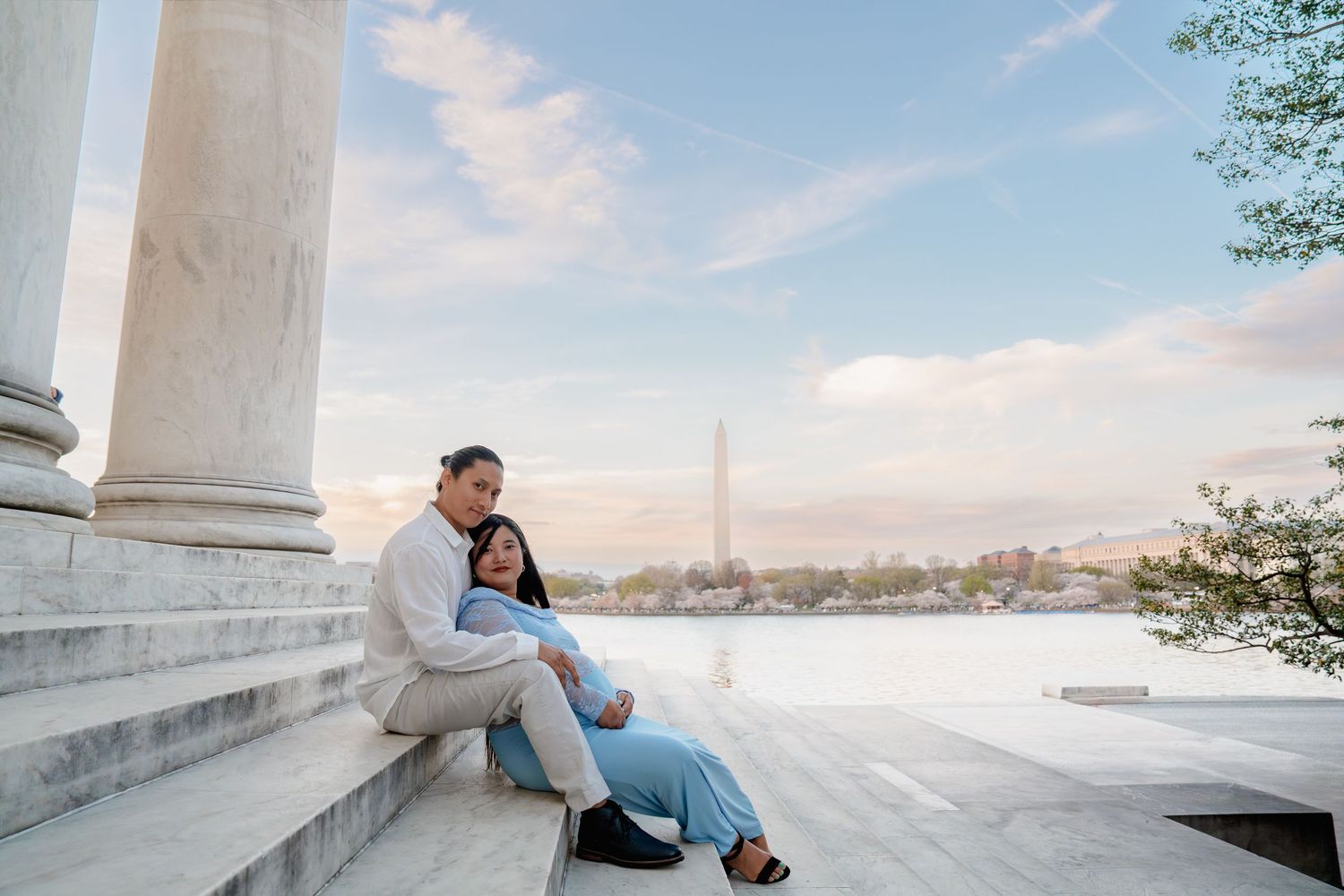 Pregnant couple sitting on marble steps at Jefferson Memorial with Washington Monument and Tidal Basin at sunset, in Washington DC