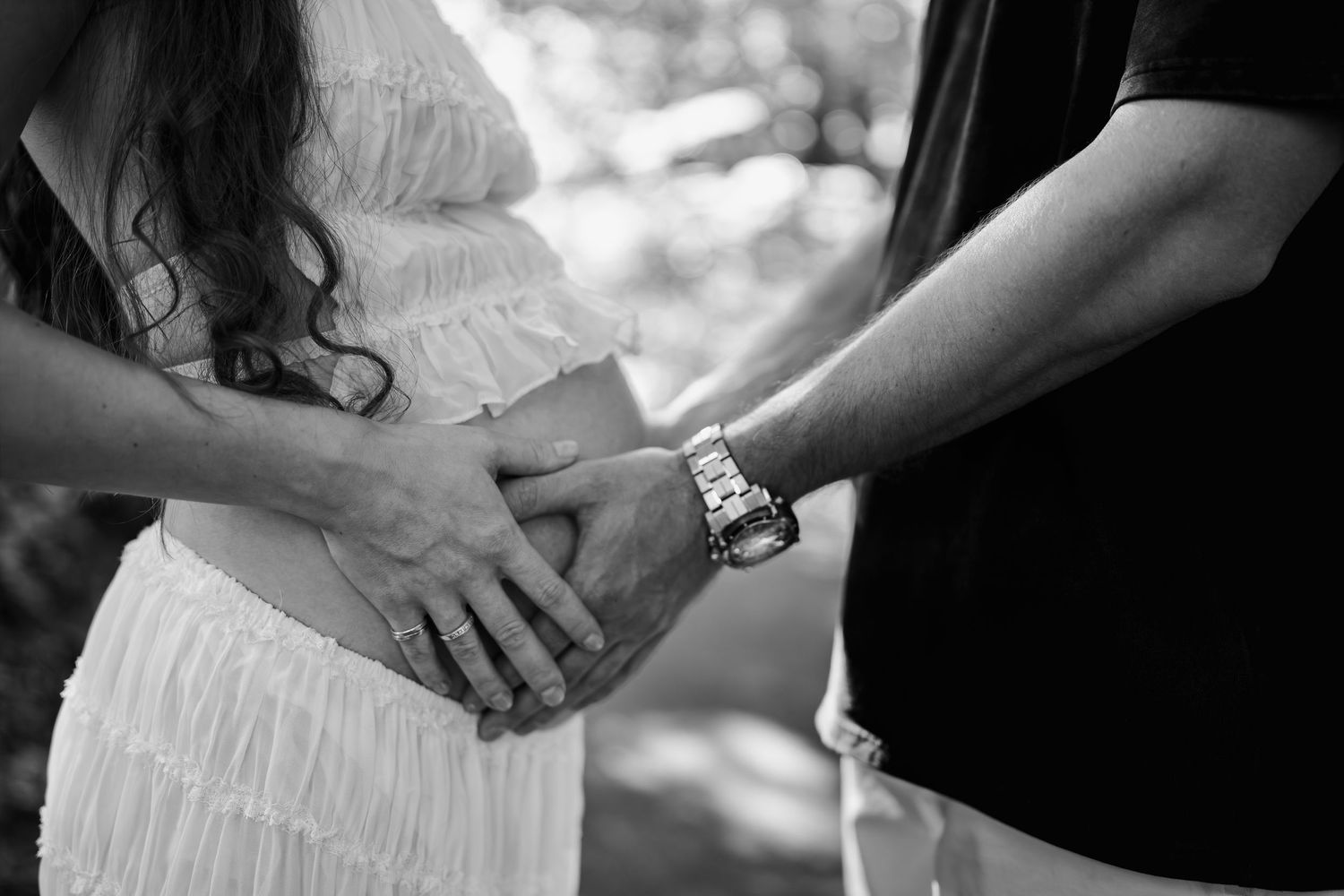 Black and white photo of a couple holding hands over a pregnant belly, capturing a tender maternity moment, in Brookside Gardens in Maryland
