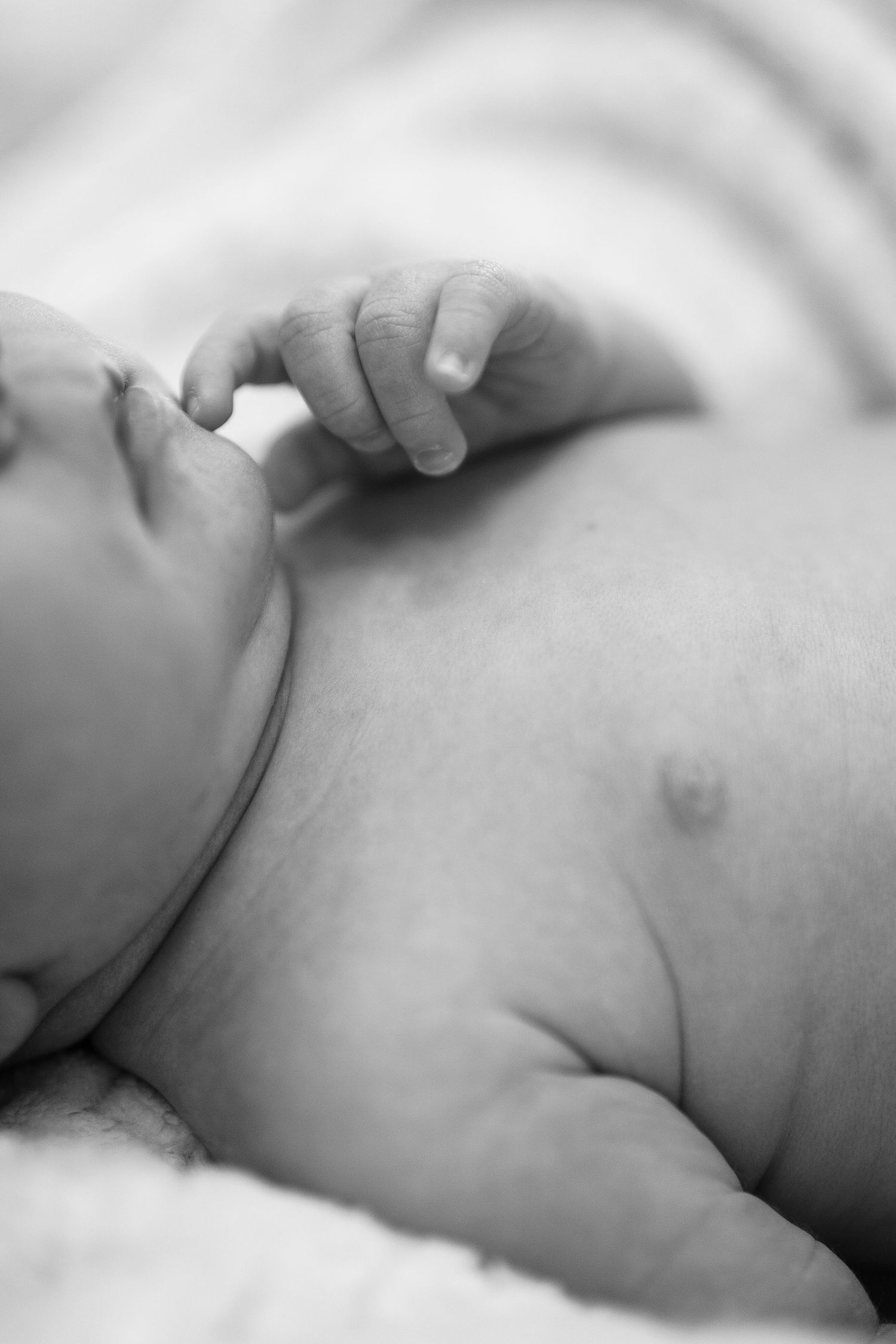 Black and white close-up of a sleeping baby's hand and chest in soft natural lighting.