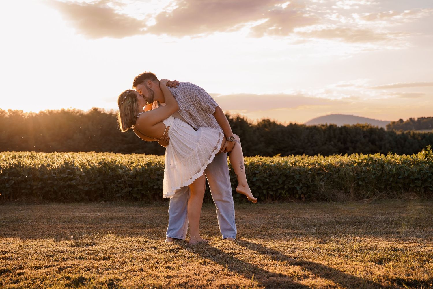 An engaged couple shares a romantic embrace in a golden field at sunset with mountains in the background, in Frederick, MD