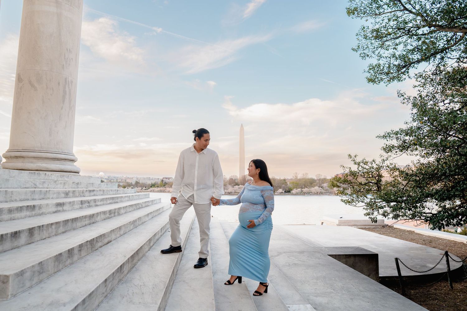 Pregnant couple holding hands on steps near Washington Monument and Tidal Basin in Washington DC.