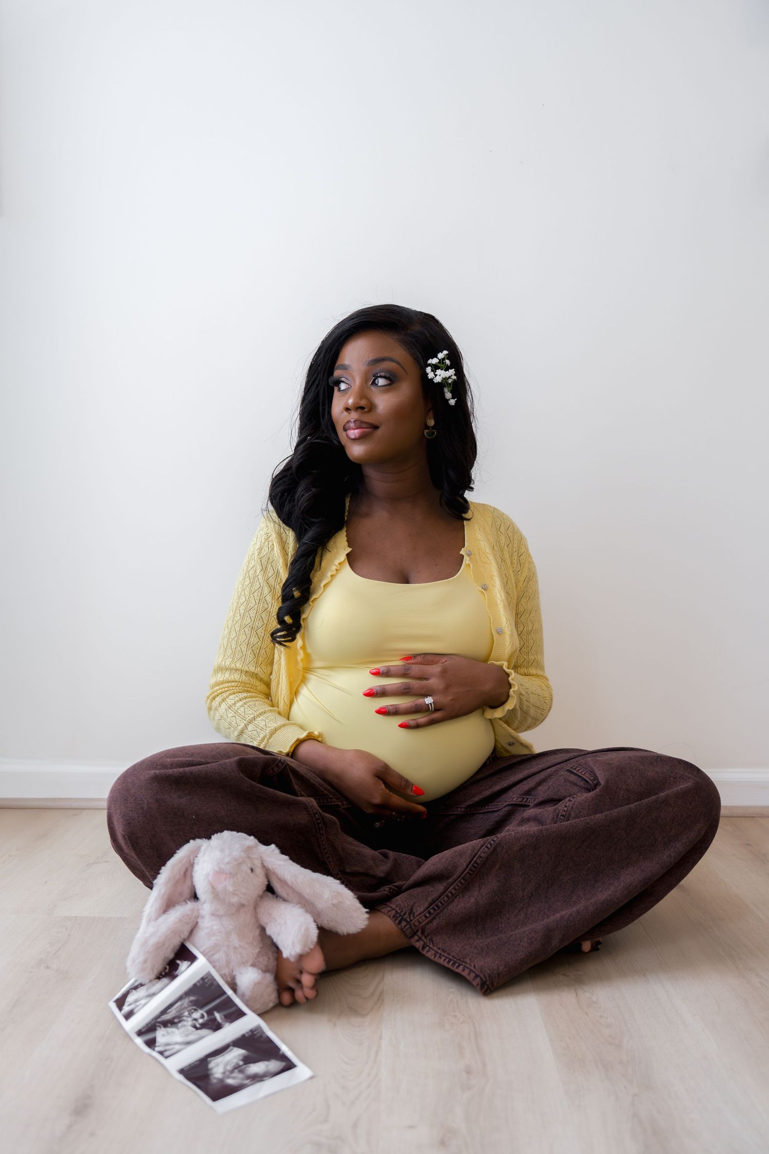 Pregnant Black woman sitting cross-legged on floor holding belly, with ultrasound photos and pink bunny toy nearby, in Ellicott City, MD