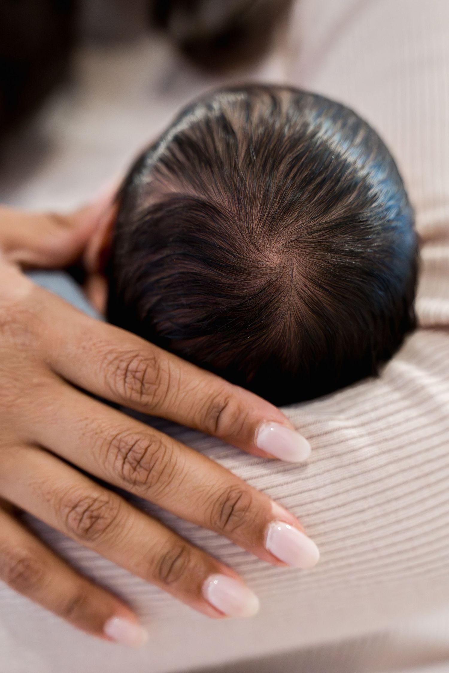 Close-up of a newborn baby's head resting on a parent's hand with pink manicured nails, in Frederick, MD