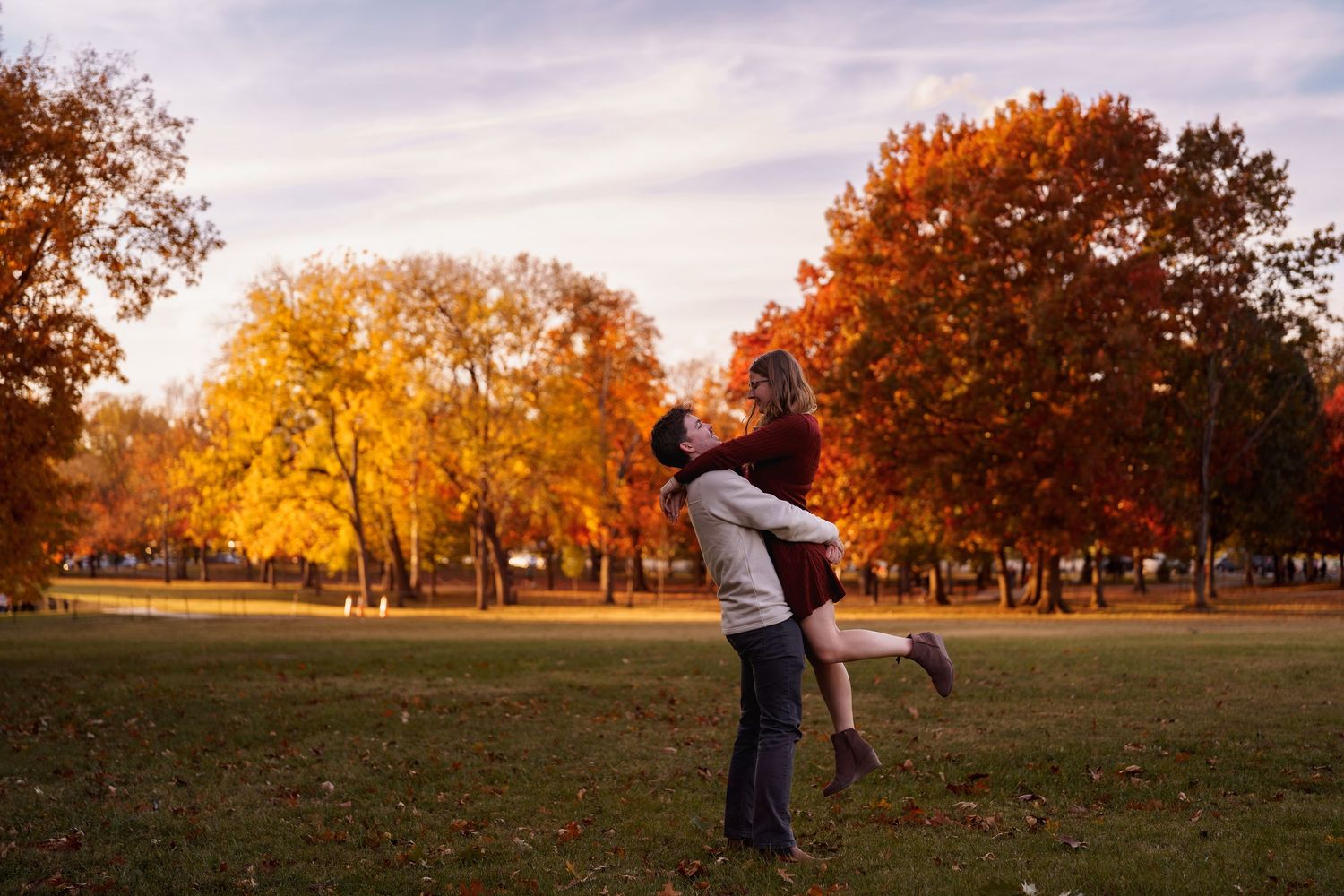 Couple embracing in a park during autumn, surrounded by vibrant orange and yellow foliage, in Constitution Gardens, DC