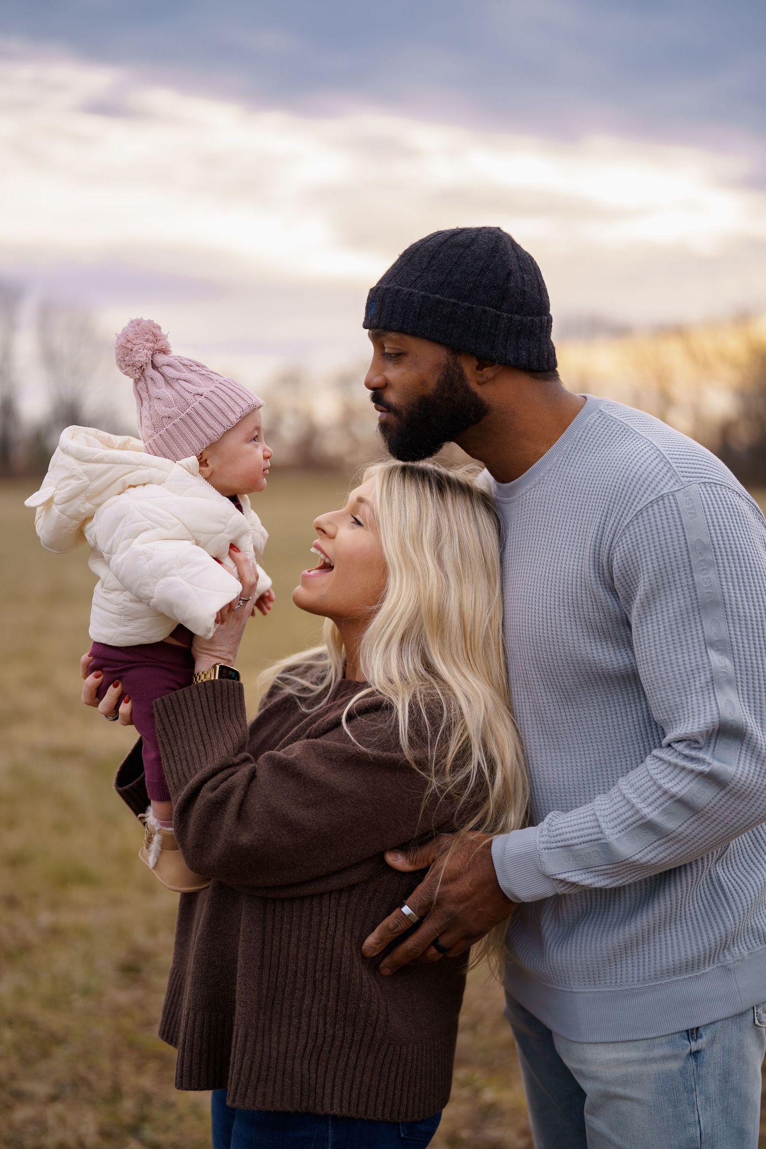 Interracial family outdoors in autumn, man and woman holding baby girl in pink hat under cloudy sky, in Frederick, MD