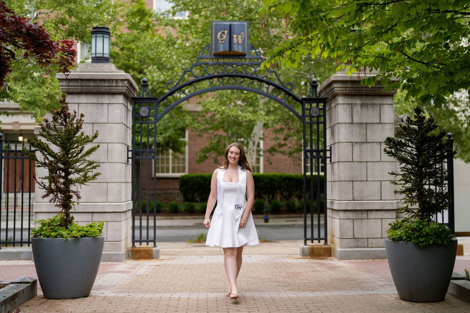 Woman in white dress walking through ornate iron gate entrance during a graduation session at GW University in Washington DC