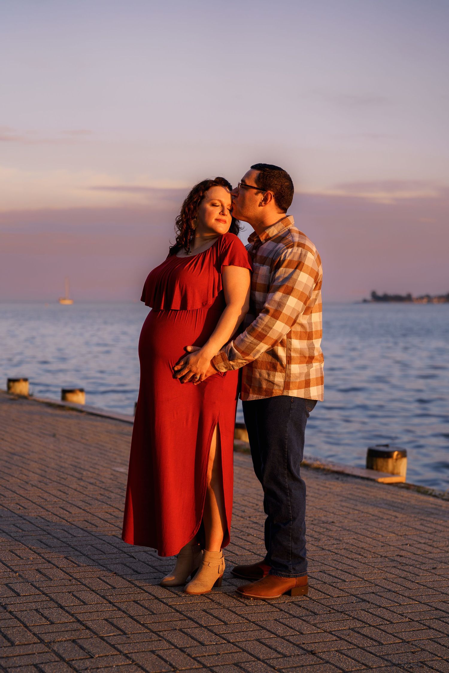 A pregnant couple embraces on a waterfront pier at sunset, during a maternity session in Annapolis, MD