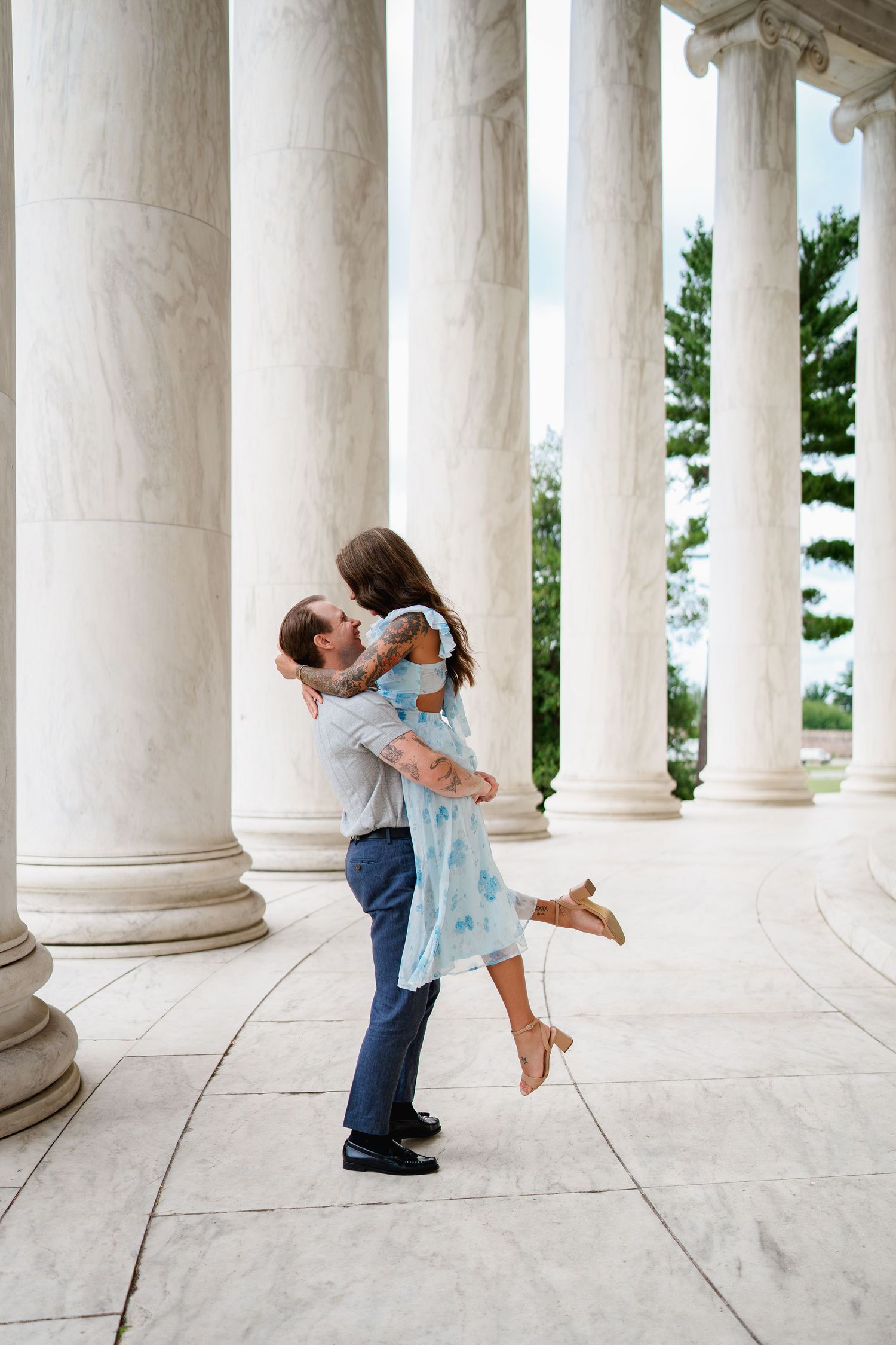 Couple sharing a romantic kiss at the Jefferson Memorial, man lifting woman in blue floral dress among marble columns, in Washington DC