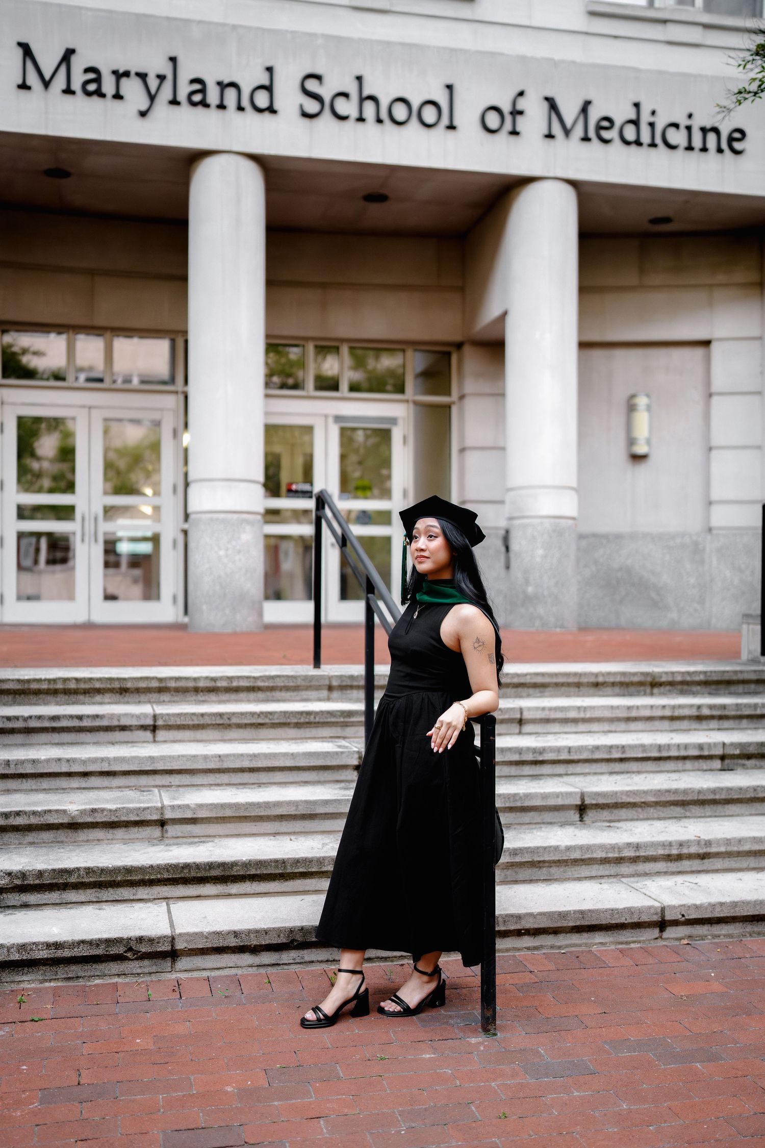 Graduate in cap and gown poses on steps of University of Maryland School of Medicine building, in Baltimore, MD