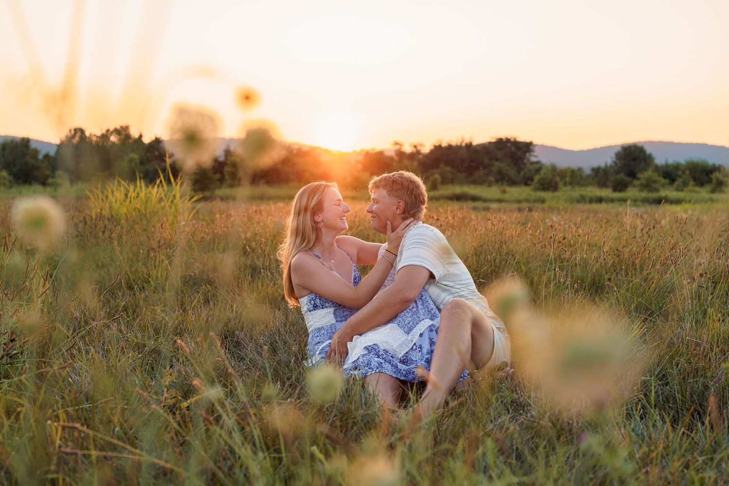 Couple sharing a romantic moment in a golden field at sunset, surrounded by wildflowers and lush greenery, in Frederick, MD