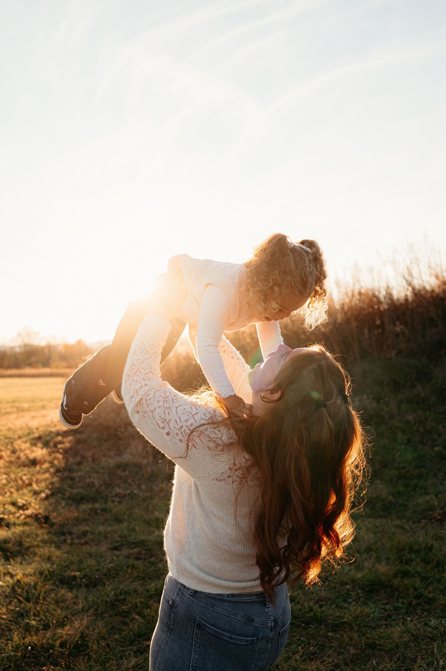 Mother lifting her toddler in the air during a golden sunset in a grassy field, in Frederick, MD