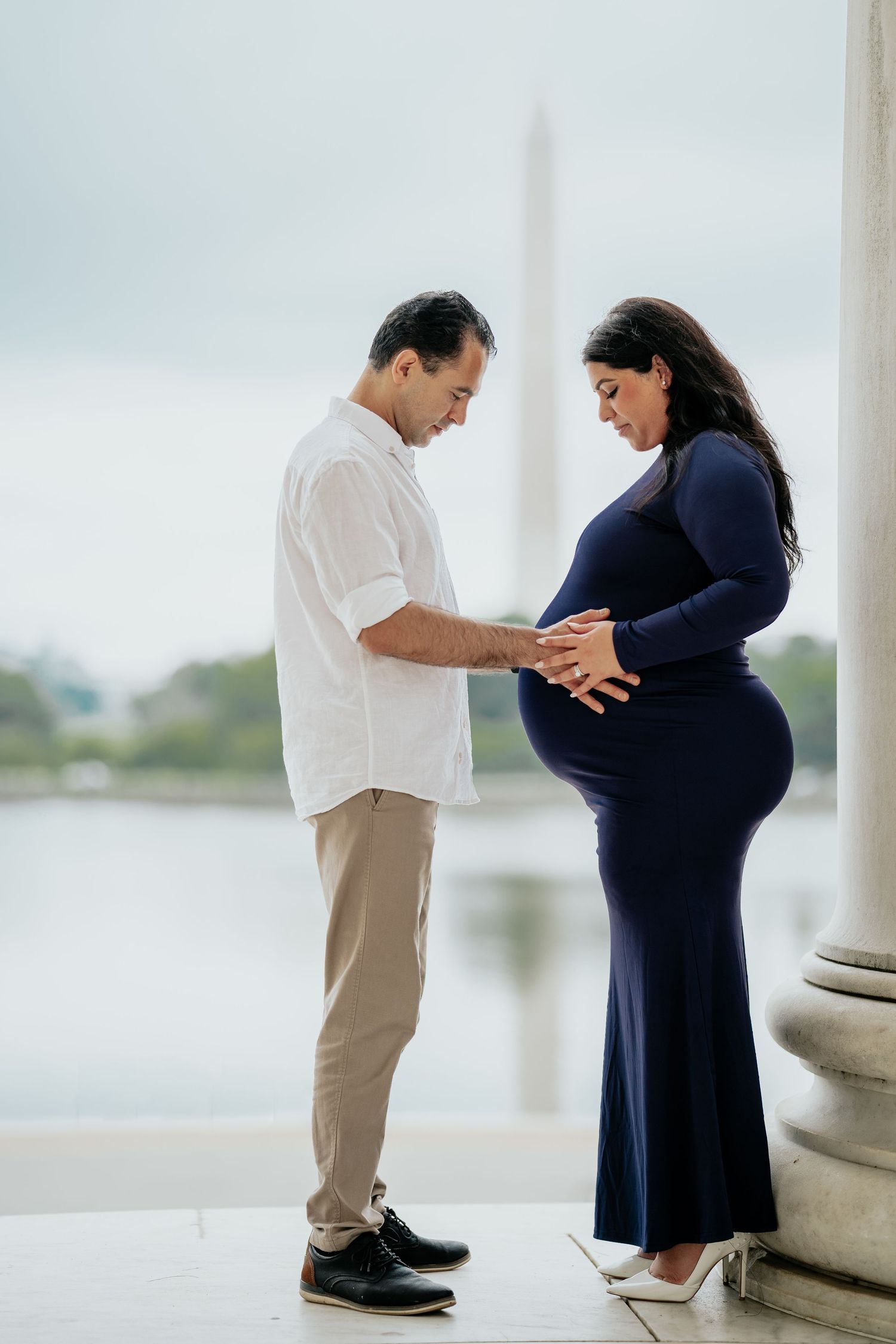 A couple shares a tender moment at the Jefferson Memorial as they touch her pregnant belly in a navy blue maternity dress, in Washington DC