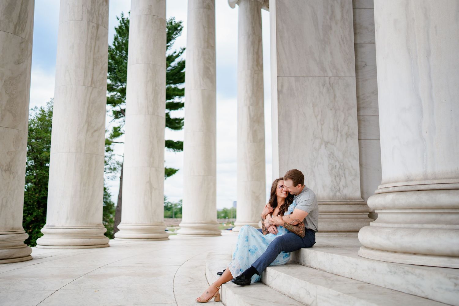 Couple sitting on marble steps embracing between grand columns at the Jefferson Memorial in Washington D.C. during an engagement session