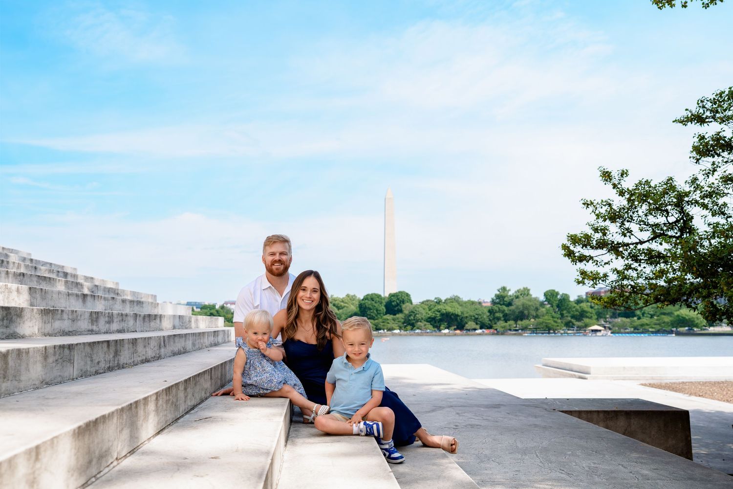 Family of four posing near the Washington Monument and Tidal Basin on sunny steps in Washington DC.