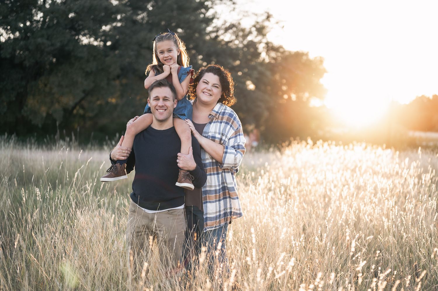 A family portrait in a sun-drenched field with tall grass during golden hour.