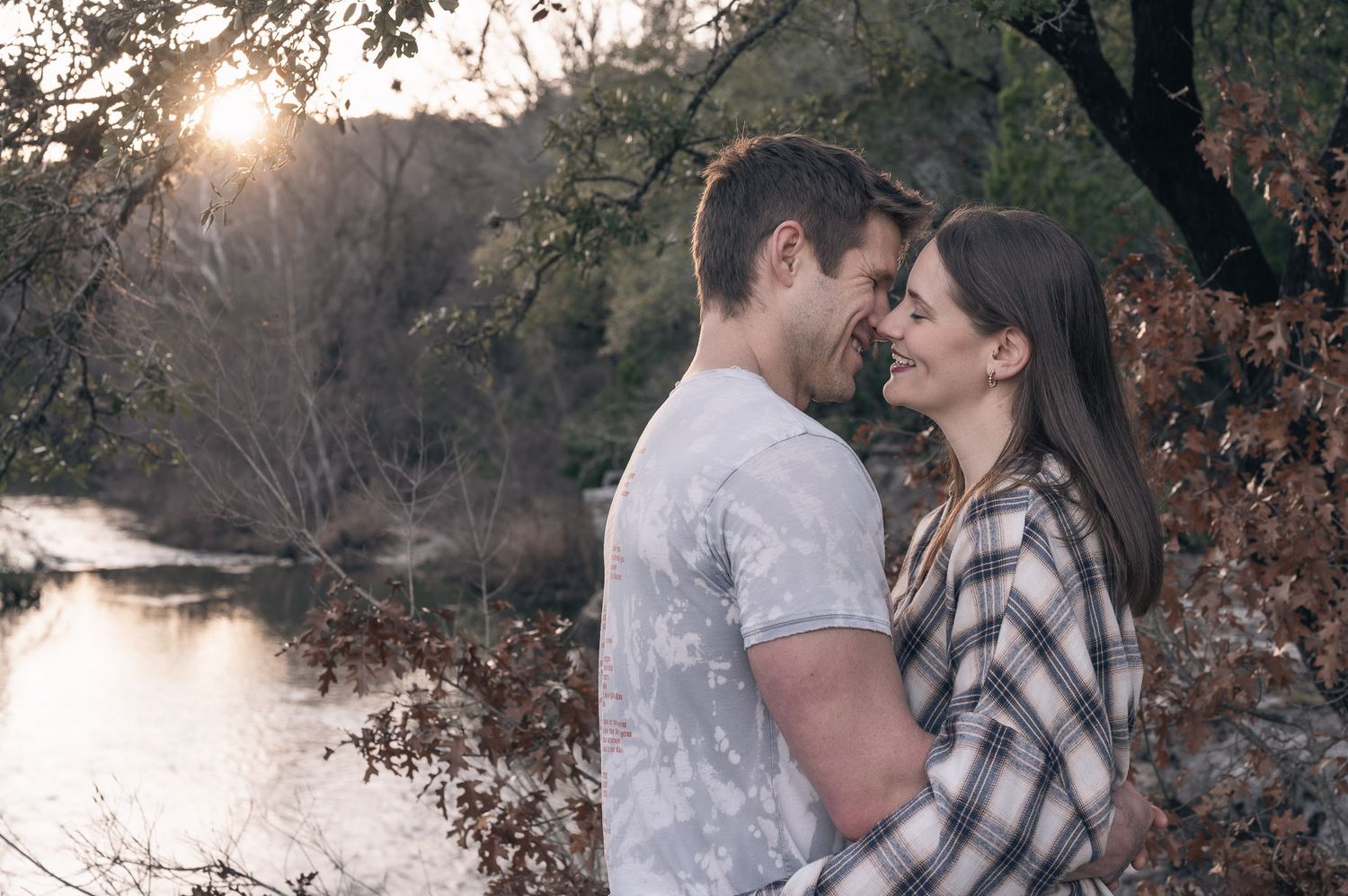 Romantic couple embracing by a lake during sunset with autumn foliage.