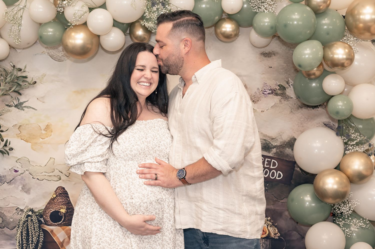A couple poses under an elegant balloon arch with sage green and gold decorations.