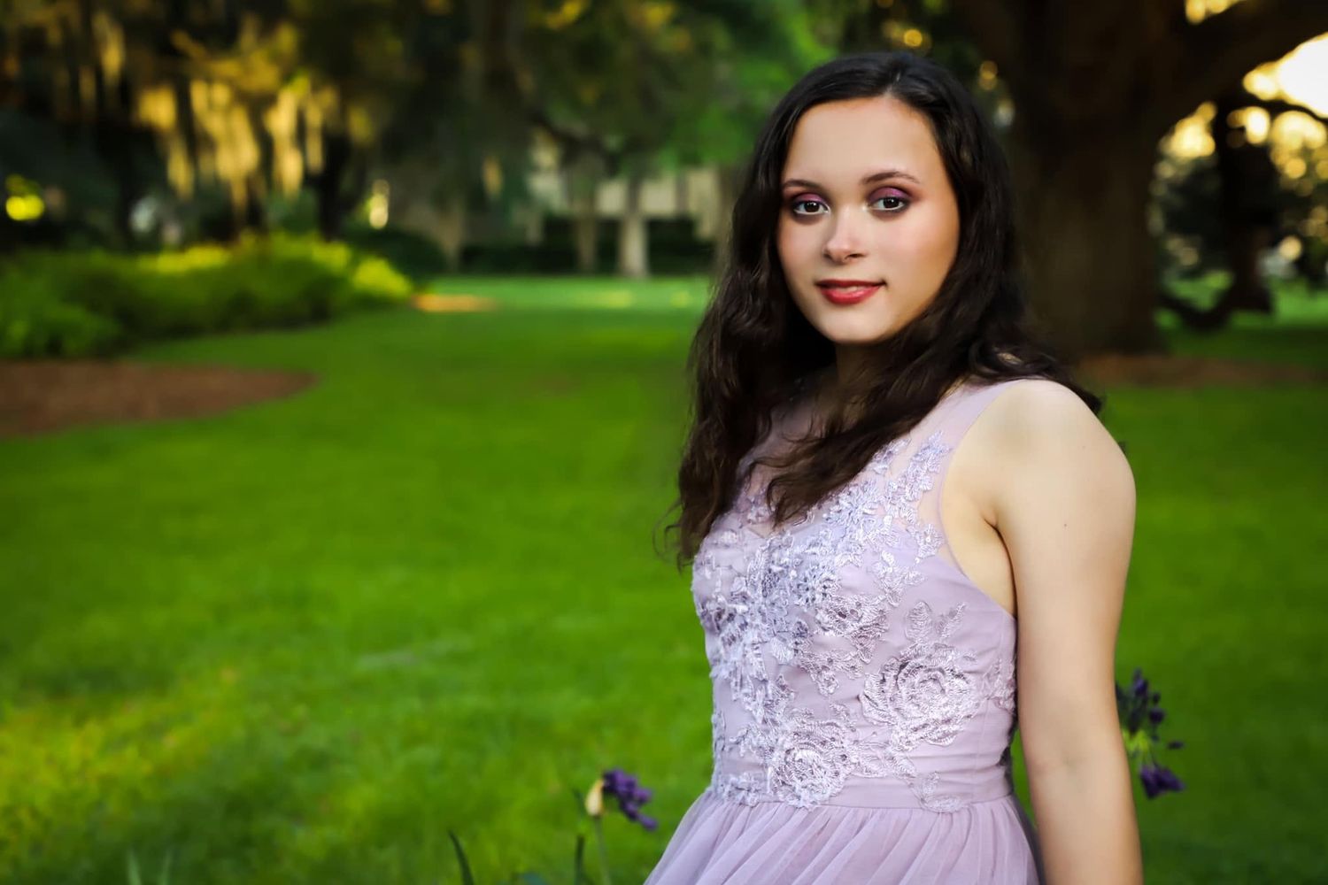 Senior portrait of a young woman in a lavender formal dress posing in a lush green park with natural light in Gainesville, Florida.