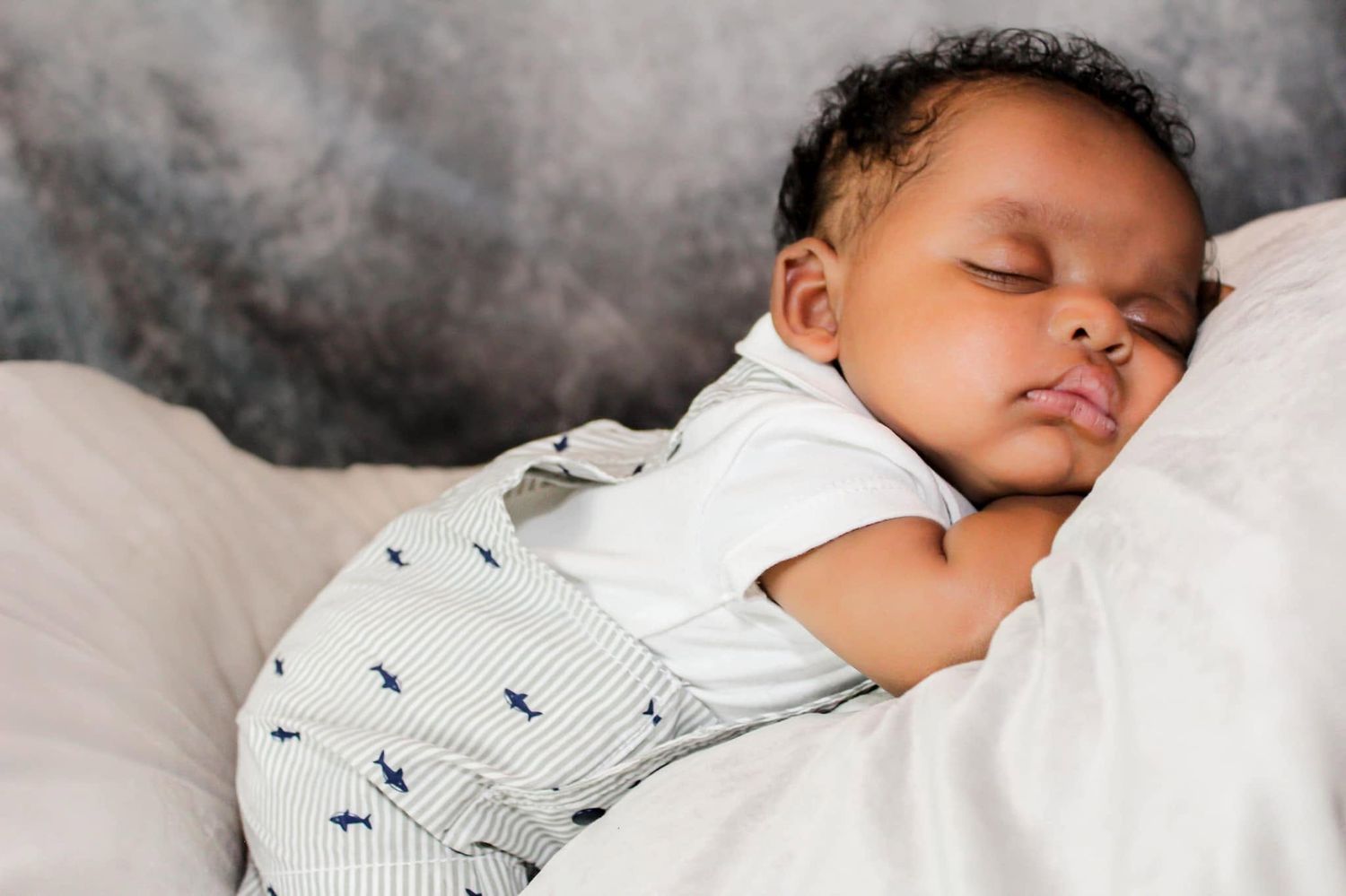 Adorable sleeping baby boy photography in striped overalls resting peacefully on white bedding in New Smyrna Florida