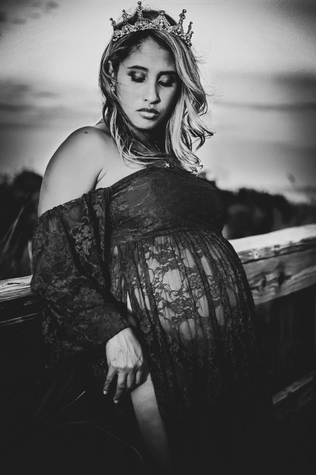 Black and white portrait of a pregnant woman in a lace dress wearing a crown, leaning on a rustic fence in Jacksonville Florida.