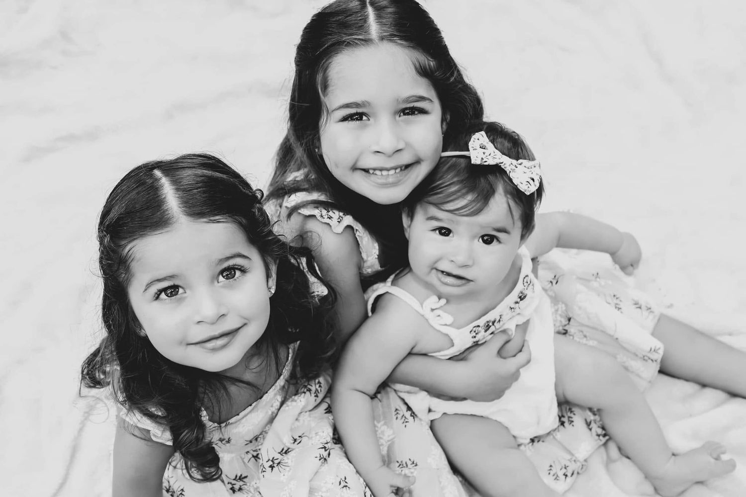Black and white portrait of three young sisters in floral dresses posing together on a white studio backdrop in Newberry, Florida