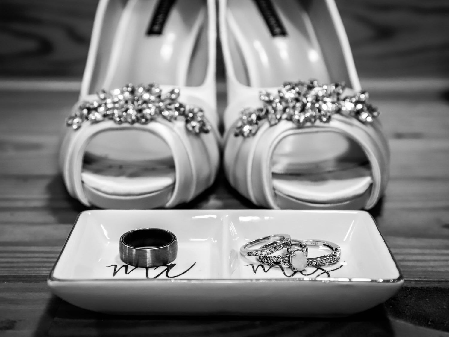 Black and white photo of jeweled bridal heels with Mr and Mrs wedding rings on decorative dish.