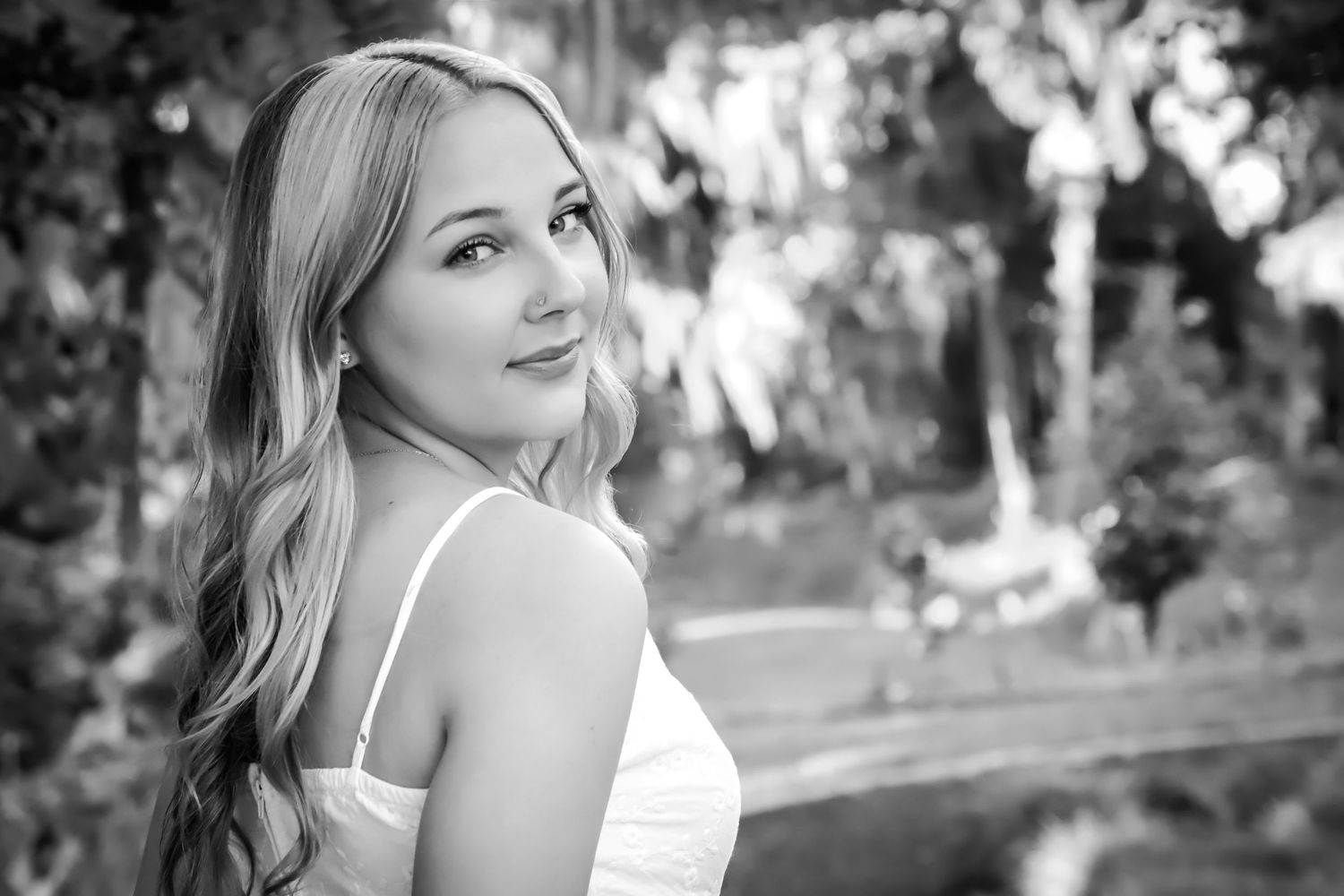 Black and white portrait of a smiling blonde woman in a white dress in a garden setting.