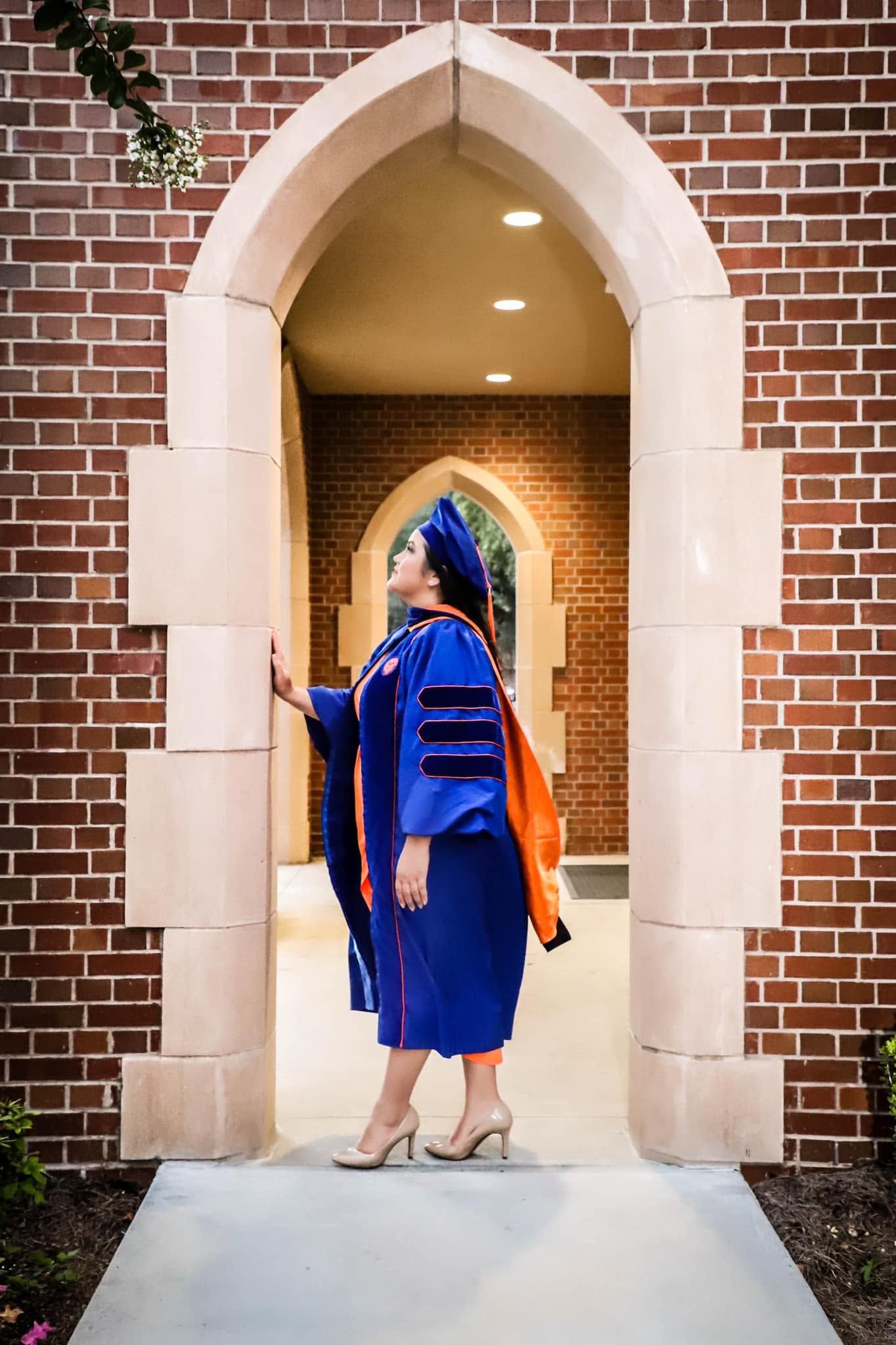 Graduation portrait of a doctoral graduate in blue regalia posing near UF’s Ben Hill Griffin Stadium in Gainesville, Florida.