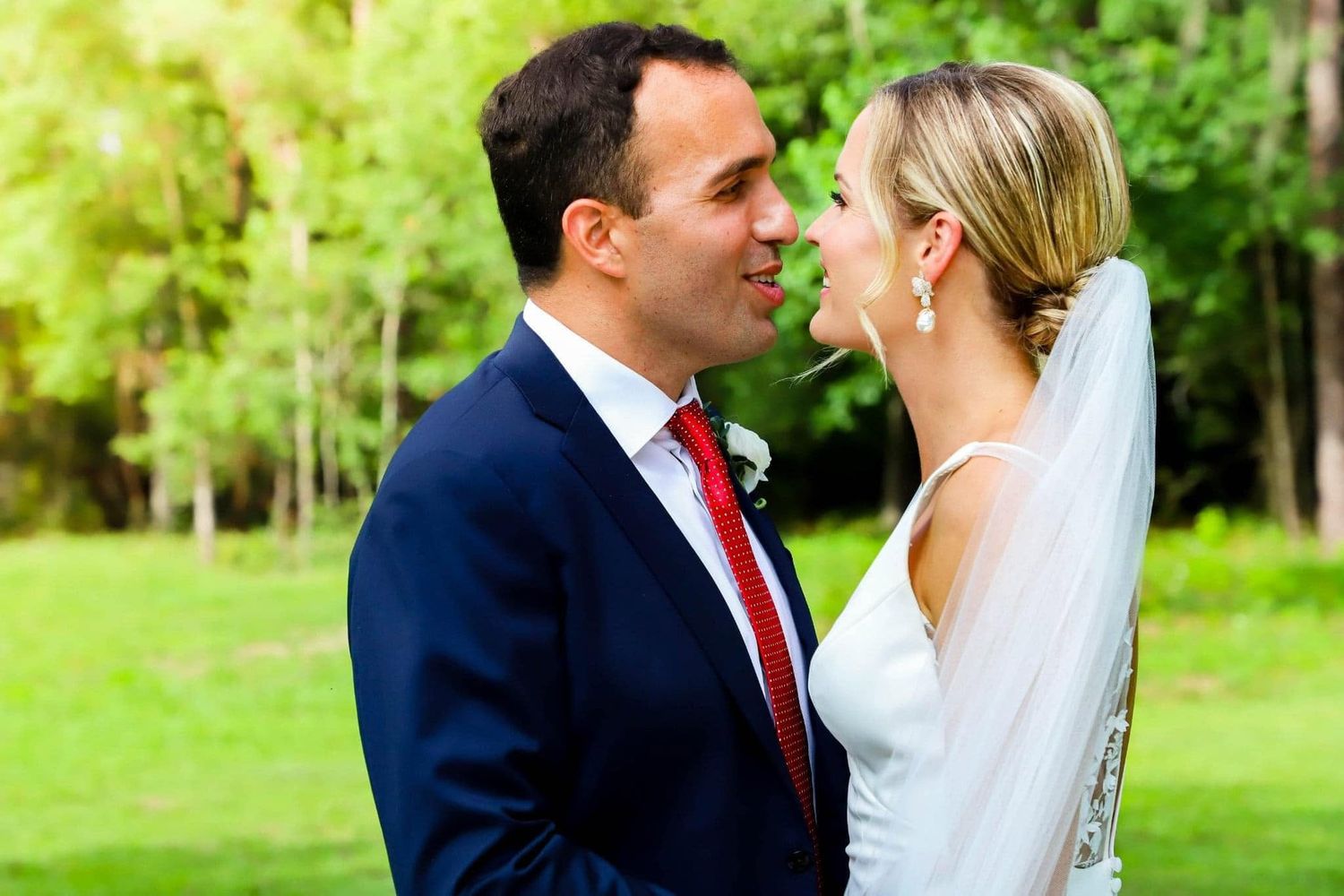 Bride and groom gazing lovingly at each other in a lush green garden setting.