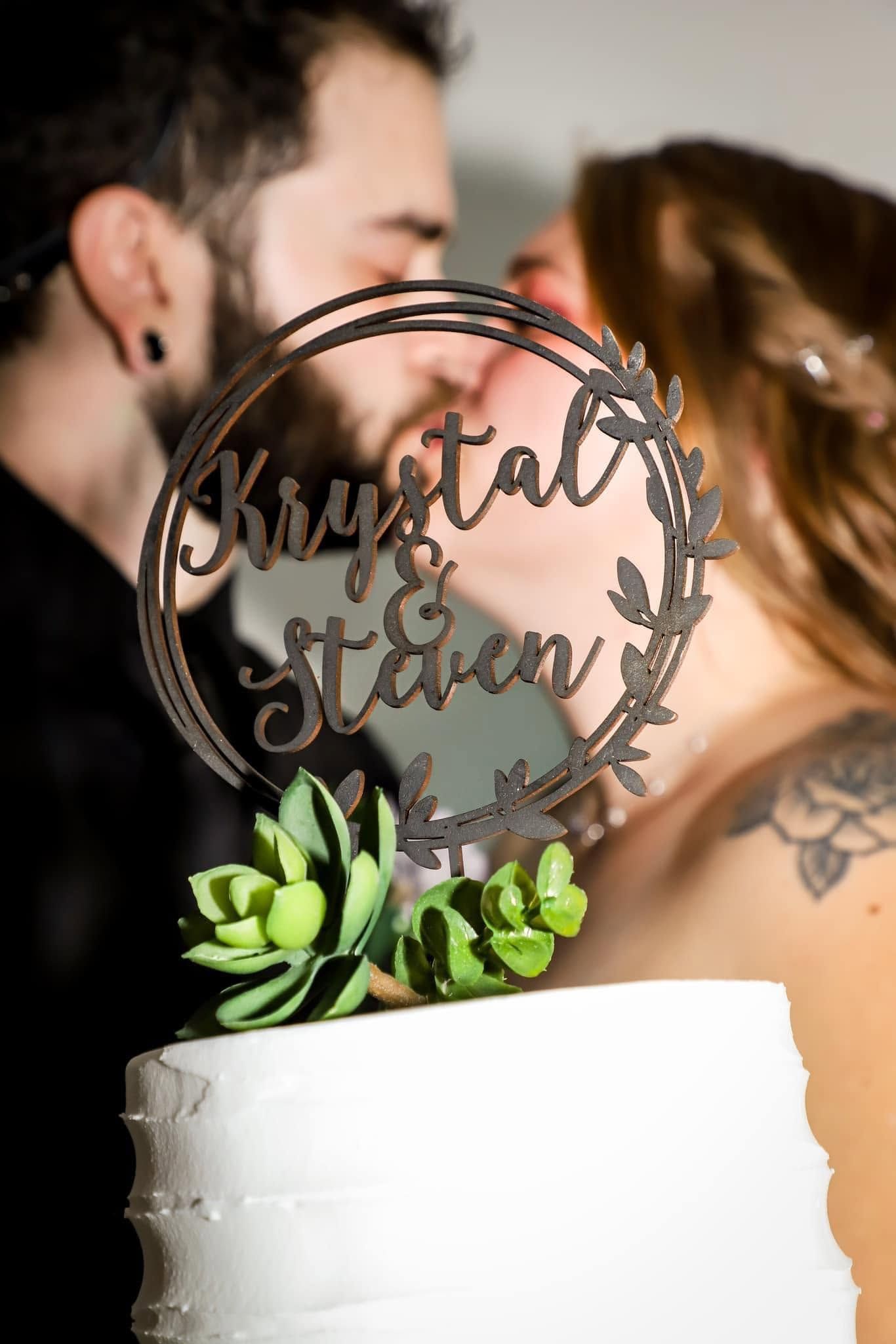 Wedding detail photo of a cake topper reading “Krystal and Steven” with succulents as the couple kisses behind it in Gainesville, Florida.
