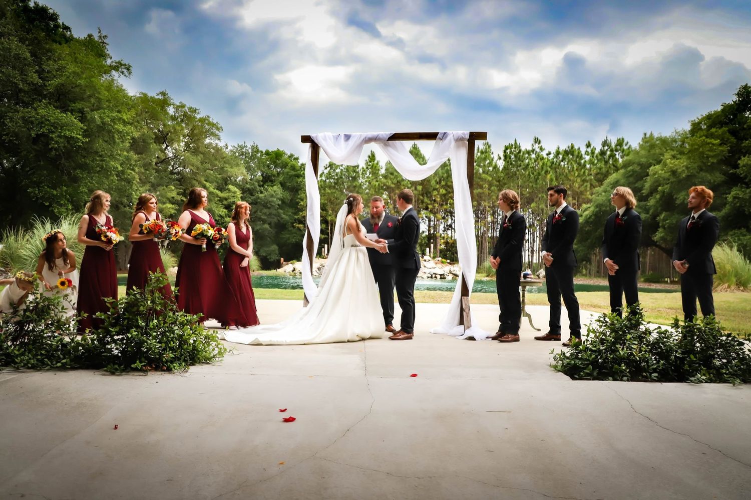 Outdoor wedding ceremony with a bridal party beneath a floral arch, with bridesmaids in burgundy dresses in Jacksonville, Florida.