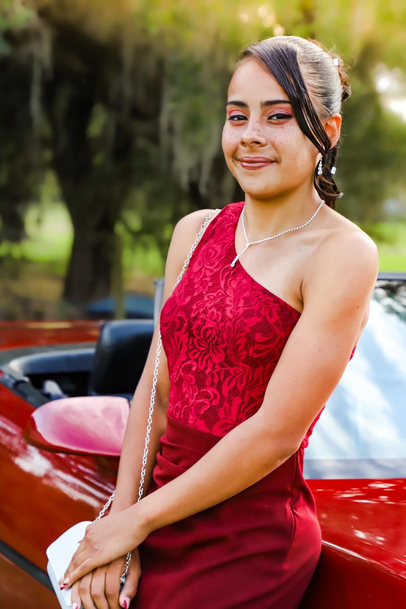 Prom session. A teenage girl in a red one-shoulder prom dress leans against a red convertible car in Newberry Florida.