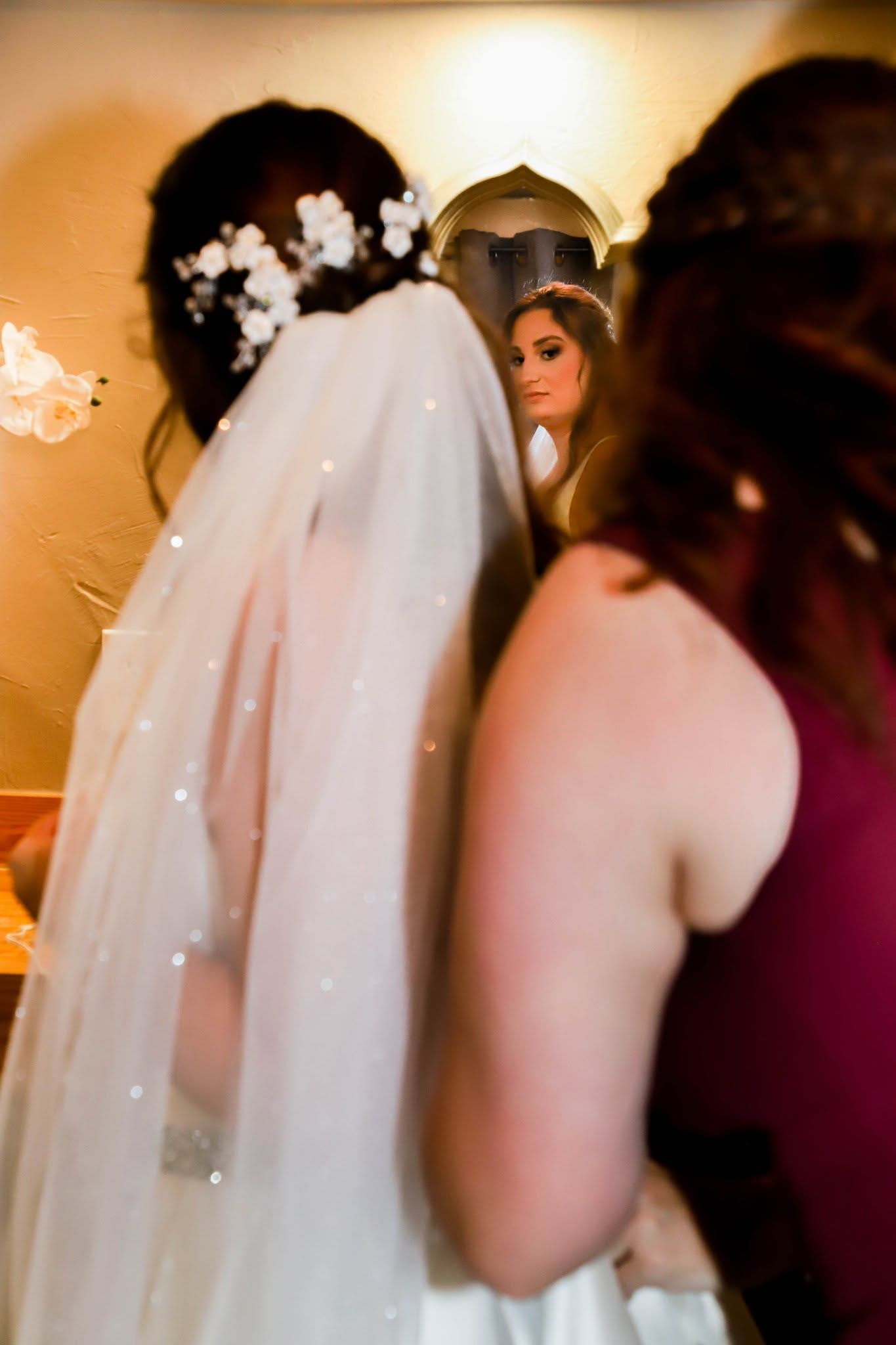 Bride in a white gown and veil with a floral hair piece reflected in a mirror beside a bridesmaid in Gainesville, Florida.