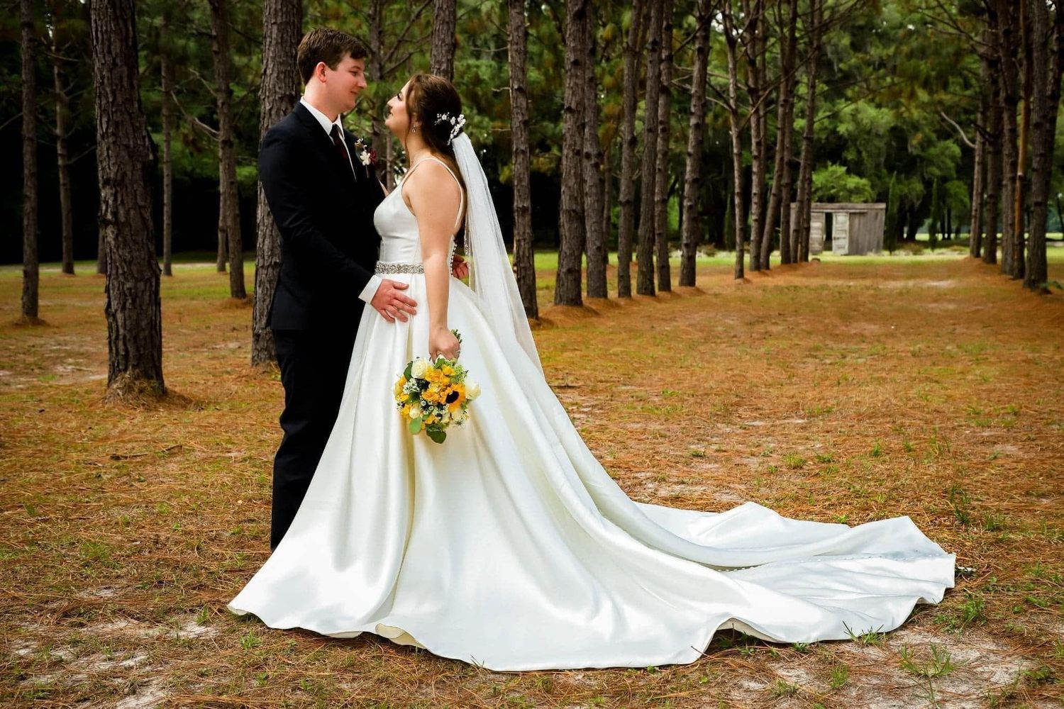 Bride and groom share a romantic moment beneath trees, with the bride in a long white gown and train in High Springs, Florida.
