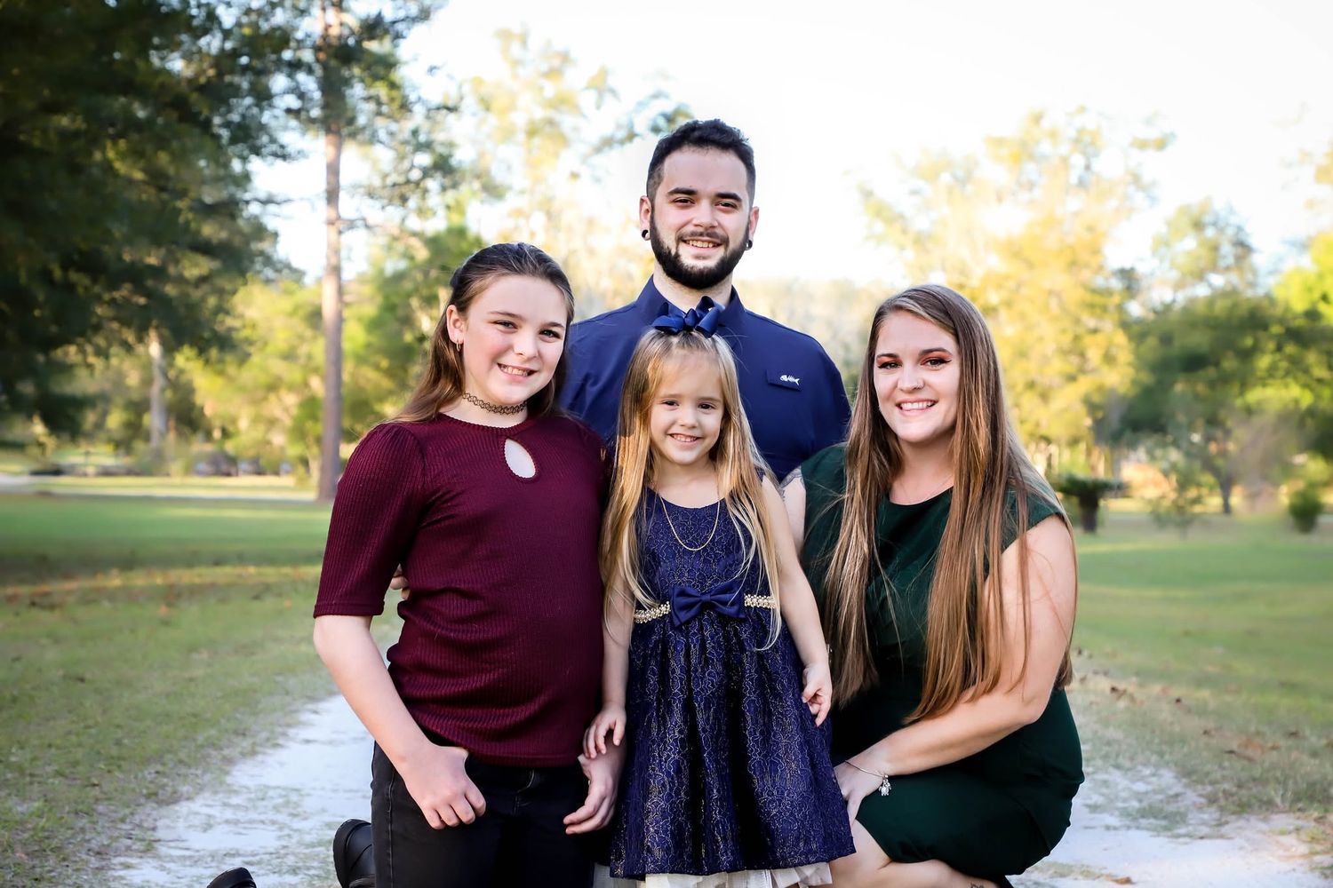Holiday mini session of a happy family of four posing outdoors in coordinated outfits at a park in Lake City, Florida.