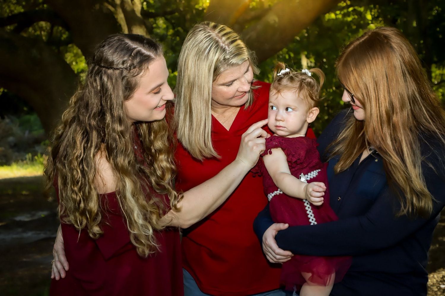 Family Generations Session. Blonde mother and two daughters admire baby girl in red dress in golden sunlit park setting.